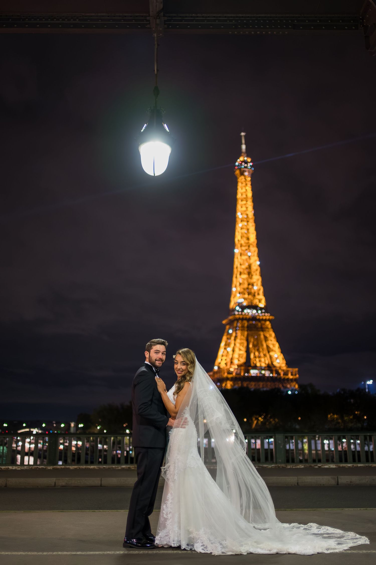 Bride and groom pose romantically in front of the illuminated Eiffel Tower at night in Paris, France.