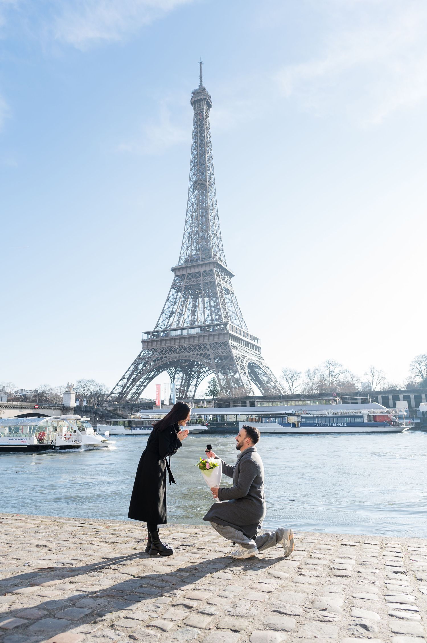 A surprise proposal moment unfolds in front of the majestic Eiffel Tower along the Seine River.