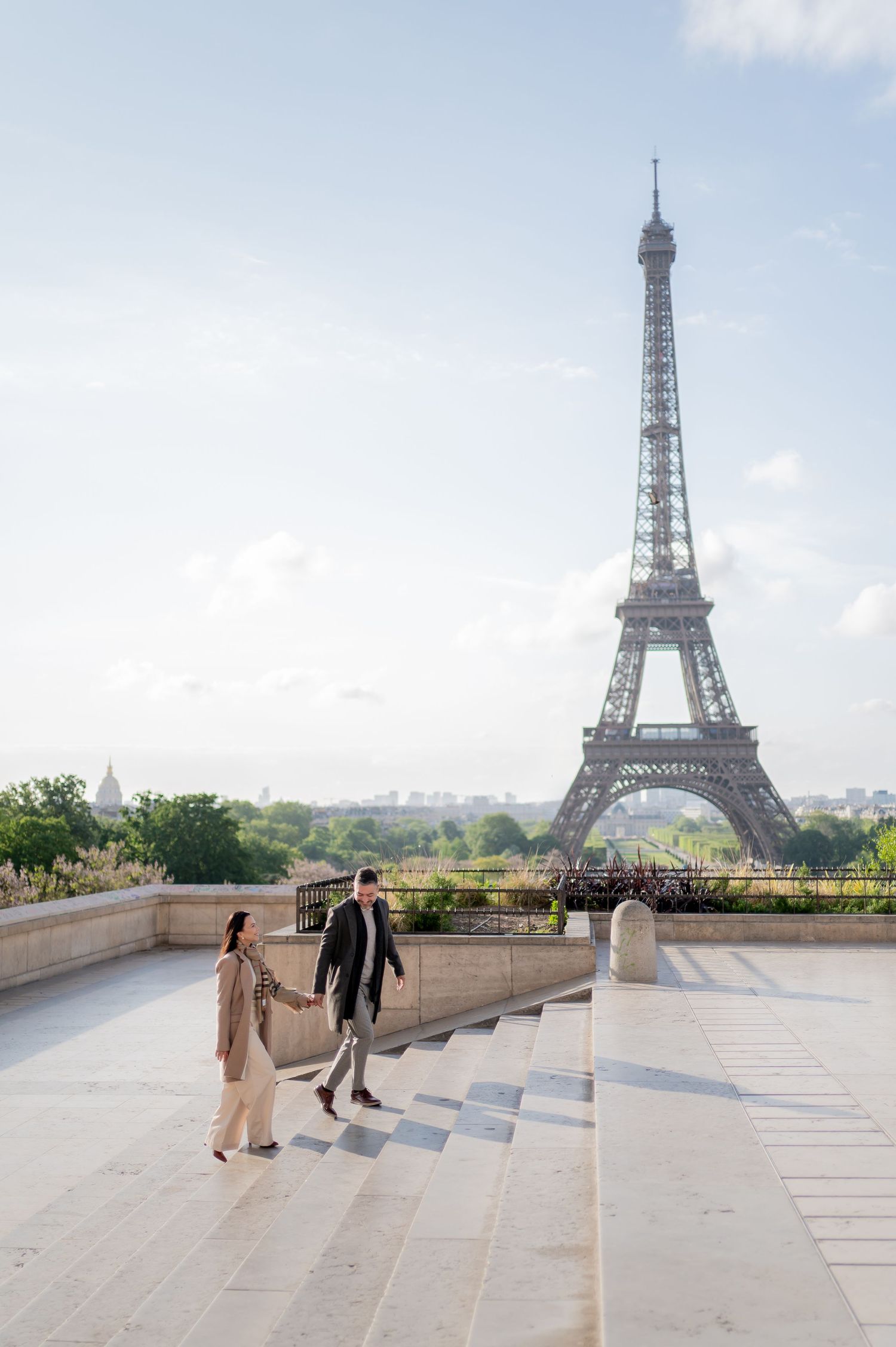 Elegant couple walking on steps with Eiffel Tower in background on sunny morning in Paris.