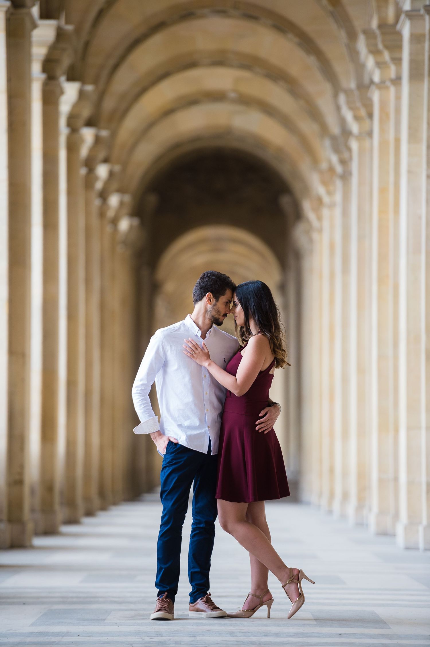 A couple shares an intimate moment in an elegant arched colonnade hallway.