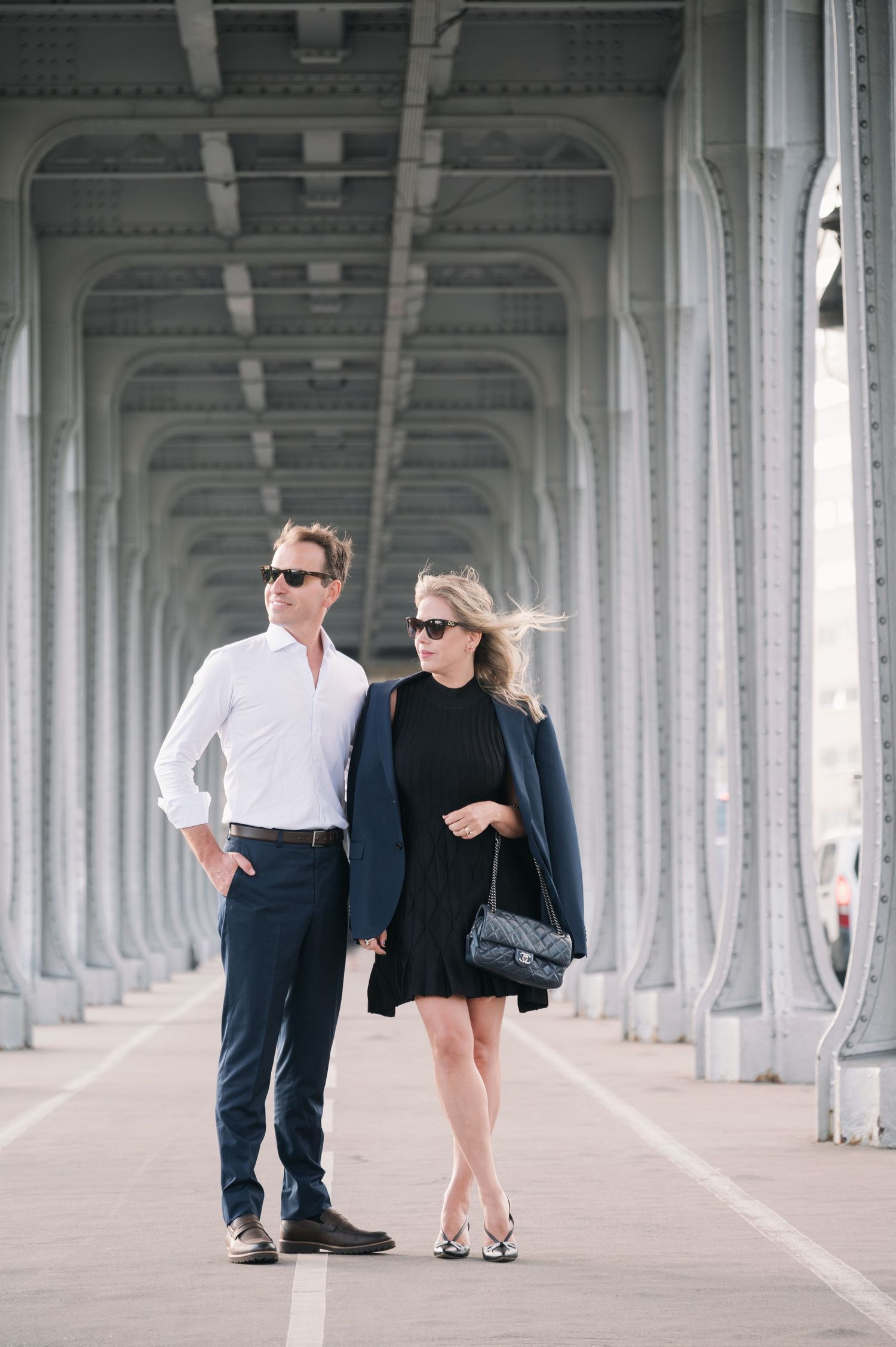 Stylish couple in sunglasses walking under Bir-Hakeim Bridge in Paris, France.