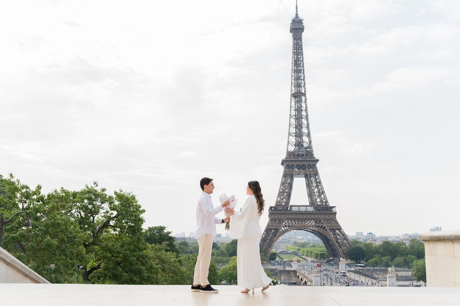 A couple shares a romantic moment in front of the iconic Eiffel Tower in Paris on a sunny day.
