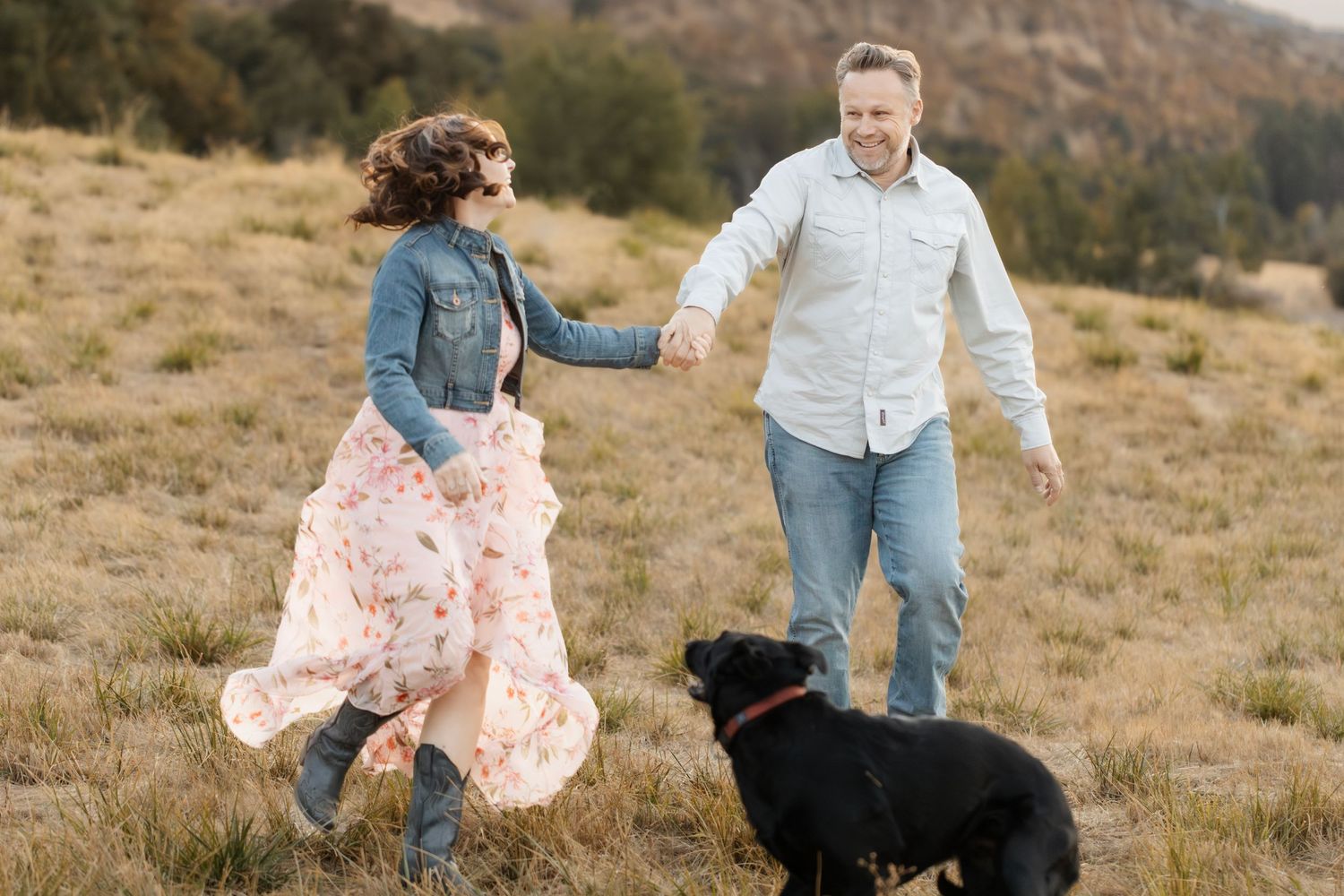 People stroll through a grassy hillside with a black dog joining them.