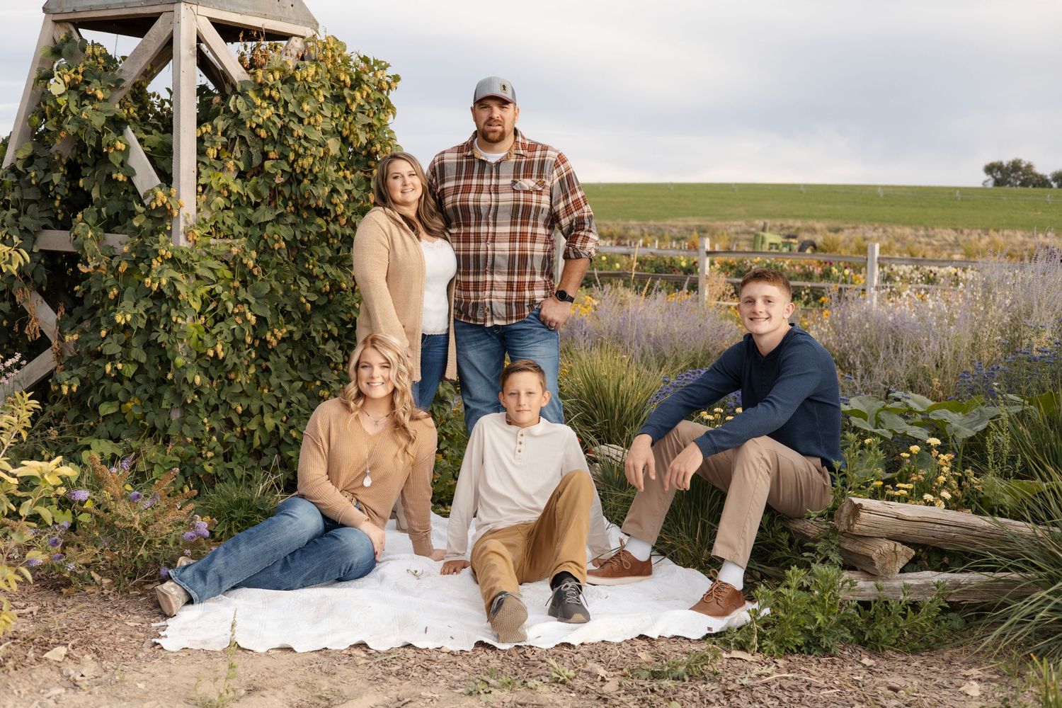 Family relaxing on blanket against rustic wooden fence in countryside setting.