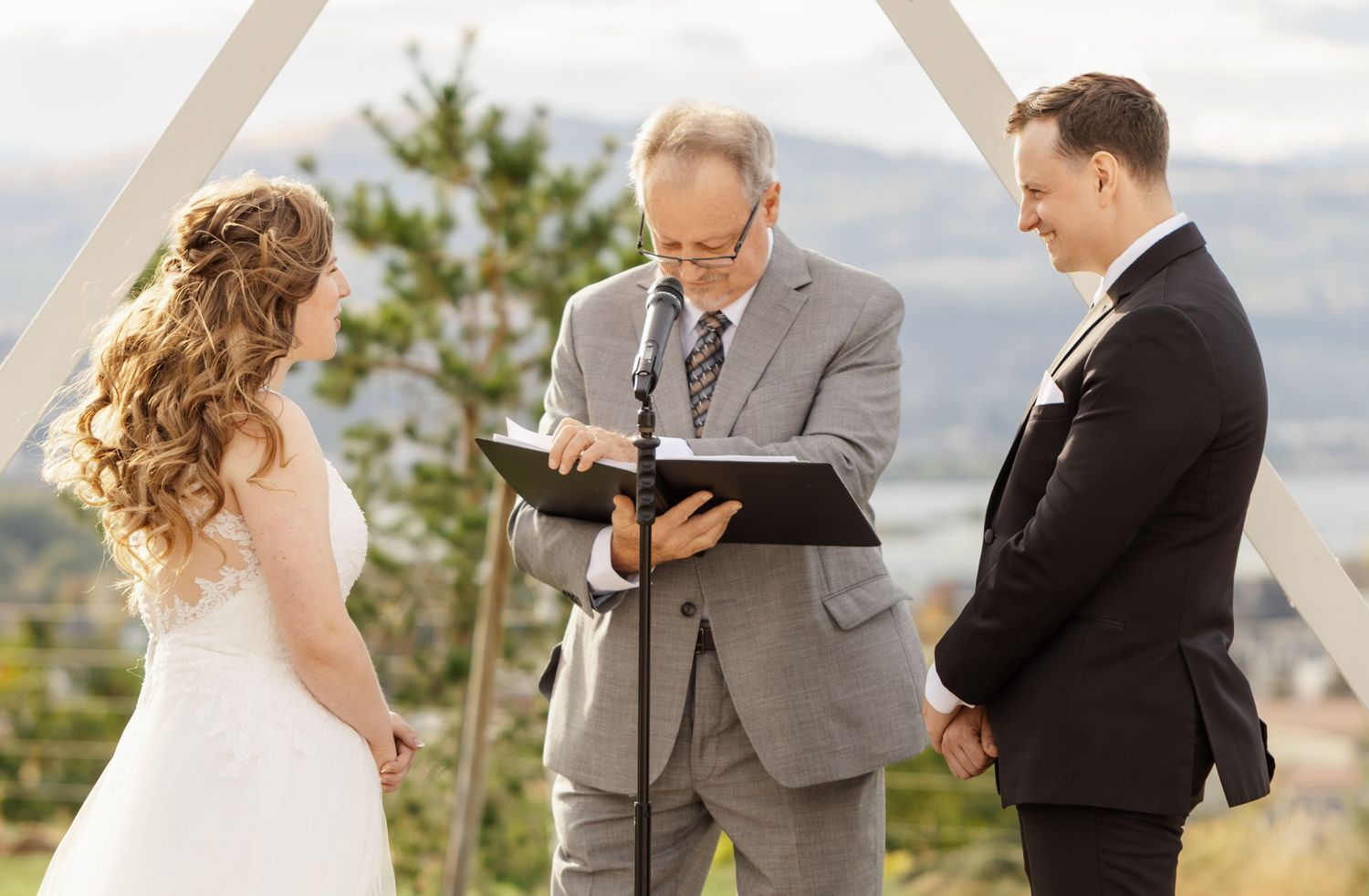 Wedding ceremony outdoors with mountains and trees in the background.