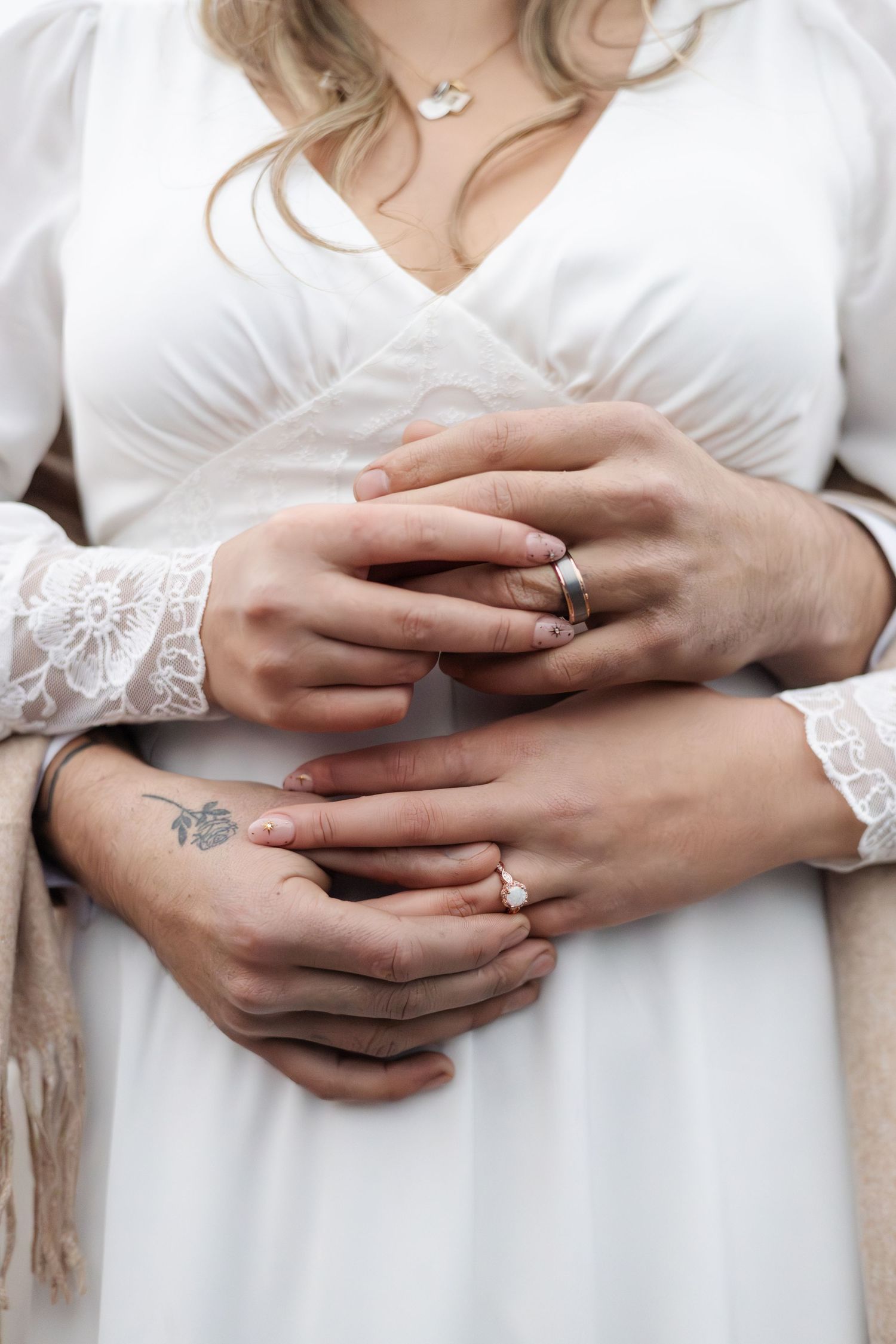 Close-up of couple's hands with wedding rings and lace sleeves.