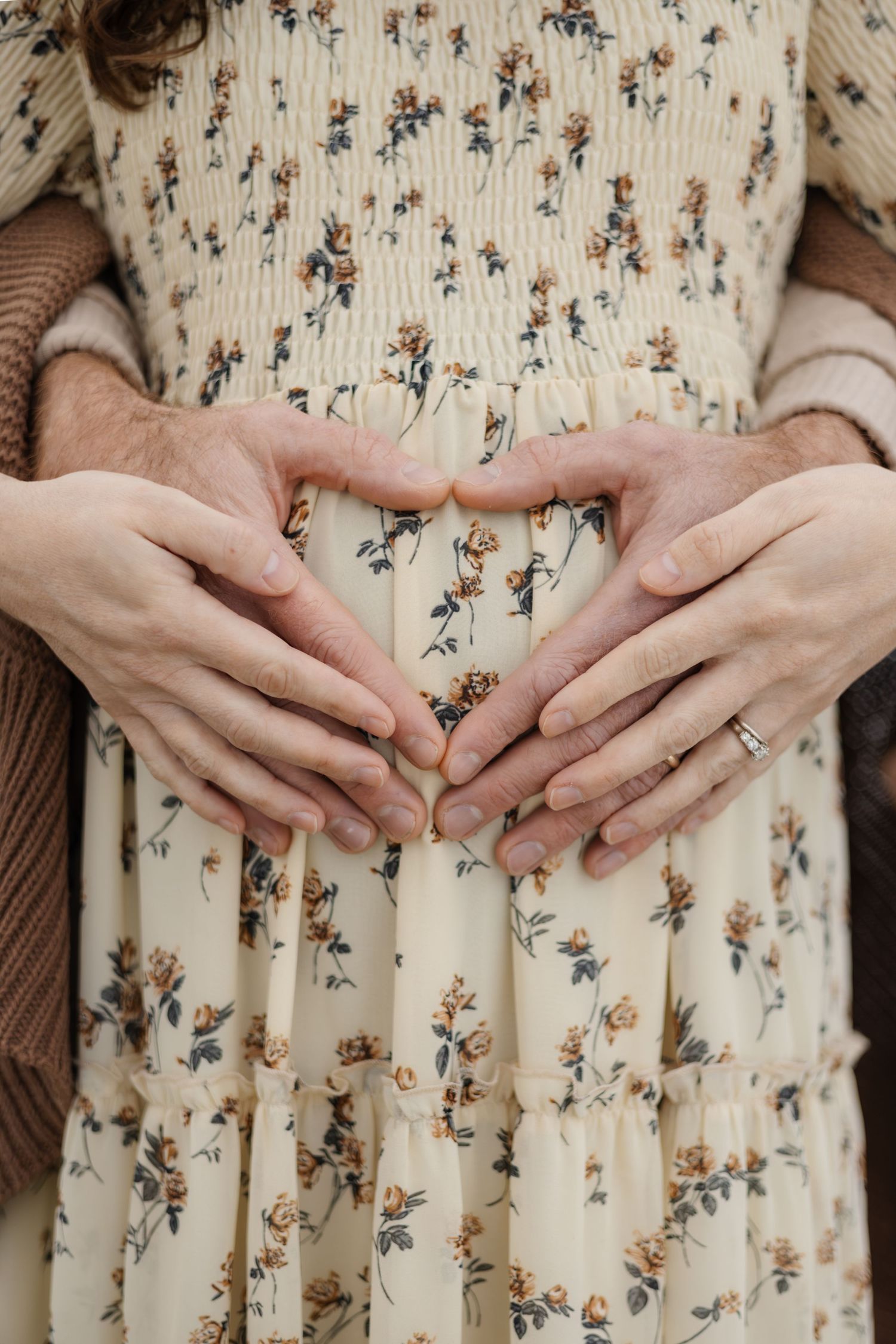 Hands forming heart shape over floral dress in maternity photo.