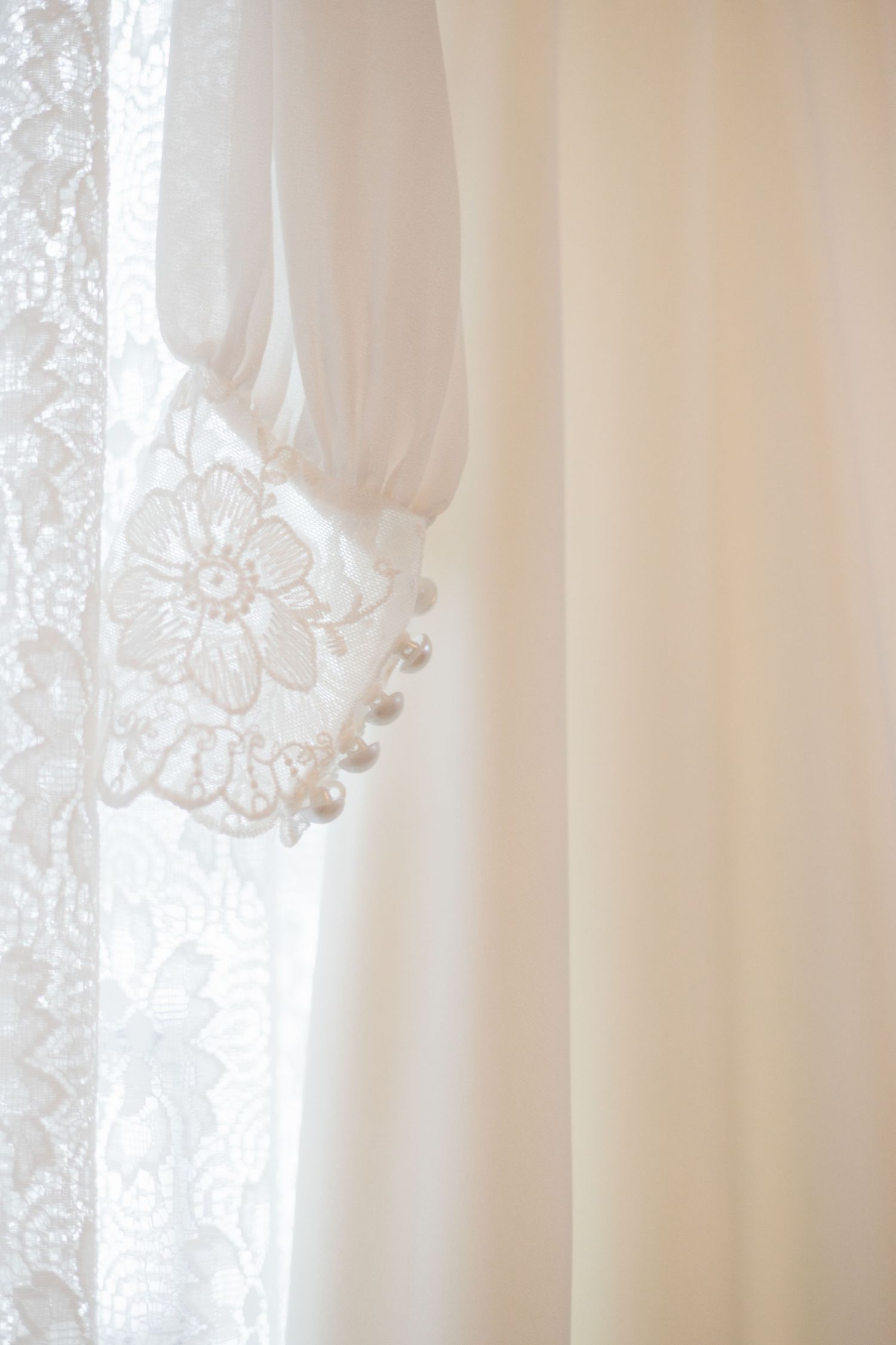 Delicate white lace curtain with floral pattern detail against soft light.