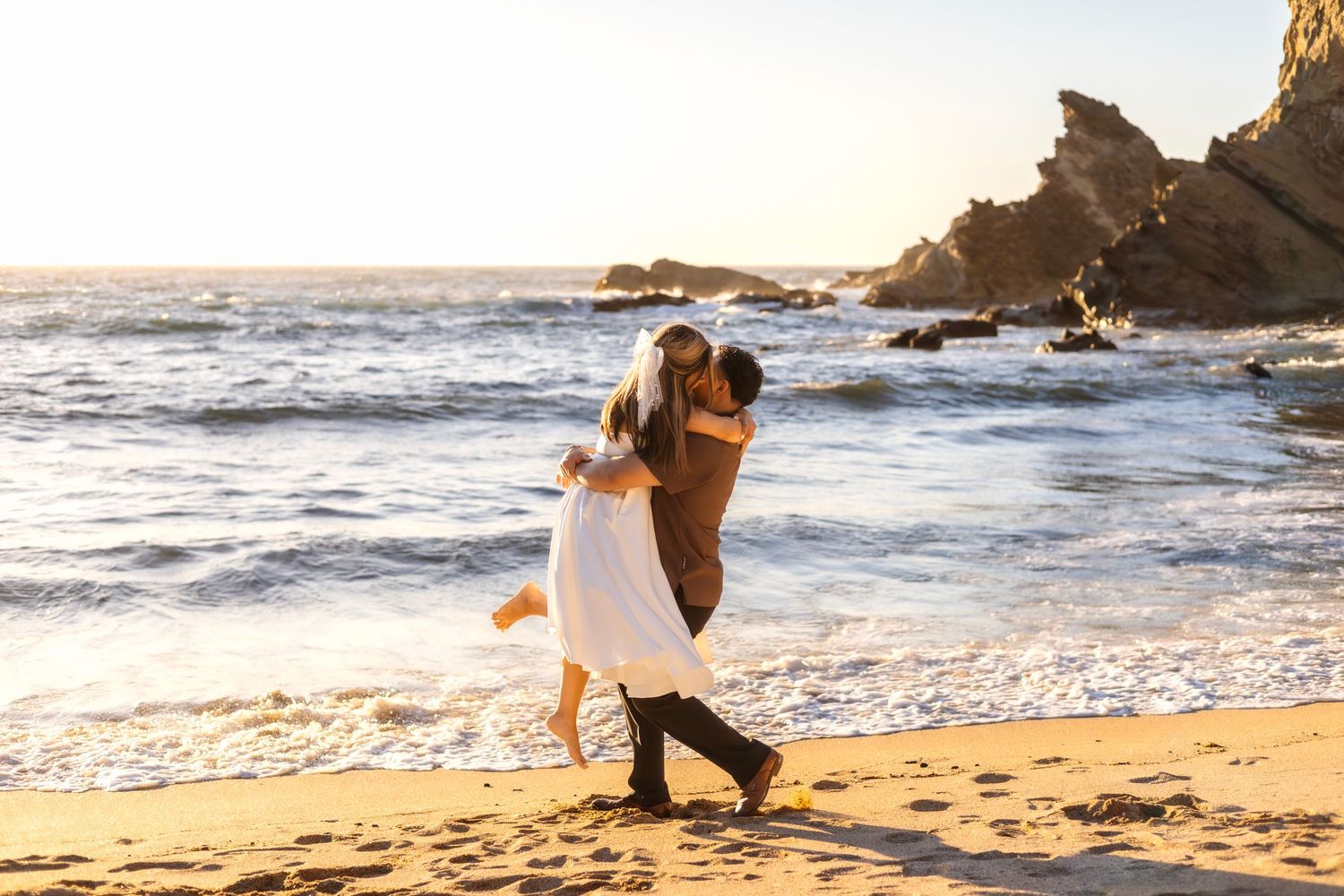 Couple sharing intimate moments on sandy beach at sunset with waves crashing.