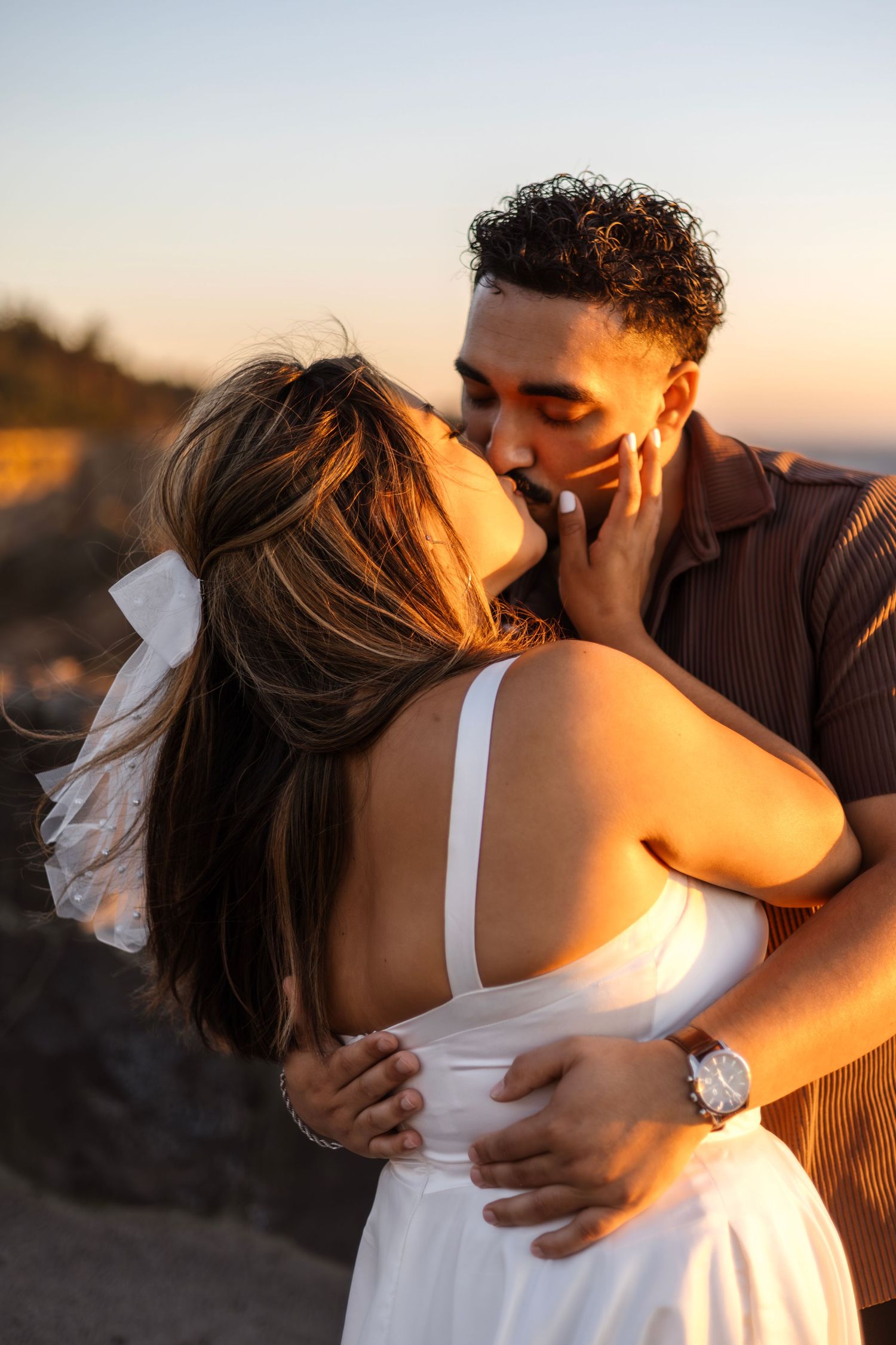 Romantic sunset embrace between couple in white dress and brown shirt.