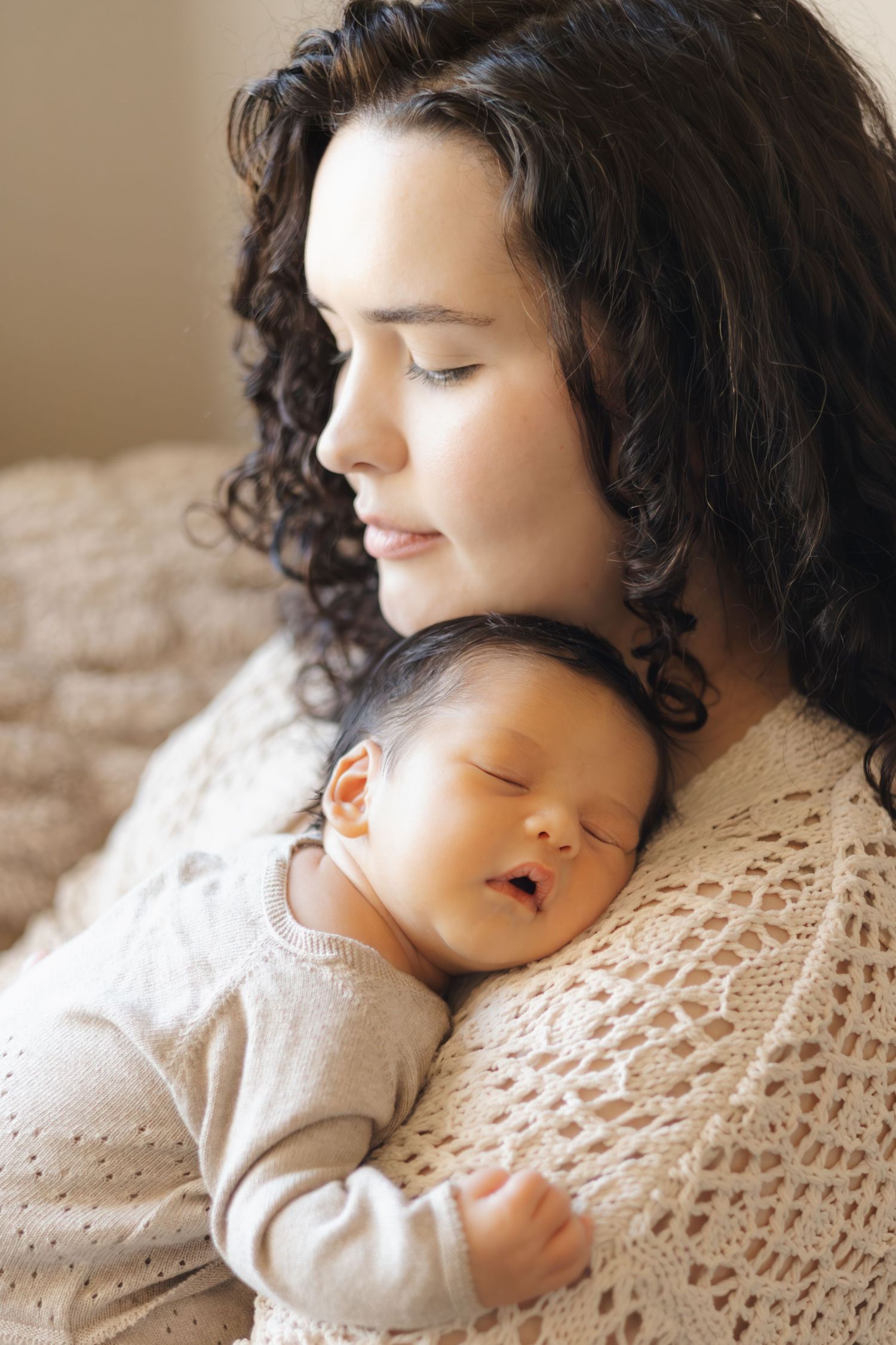 Mother and sleeping baby resting together on a crocheted blanket.
