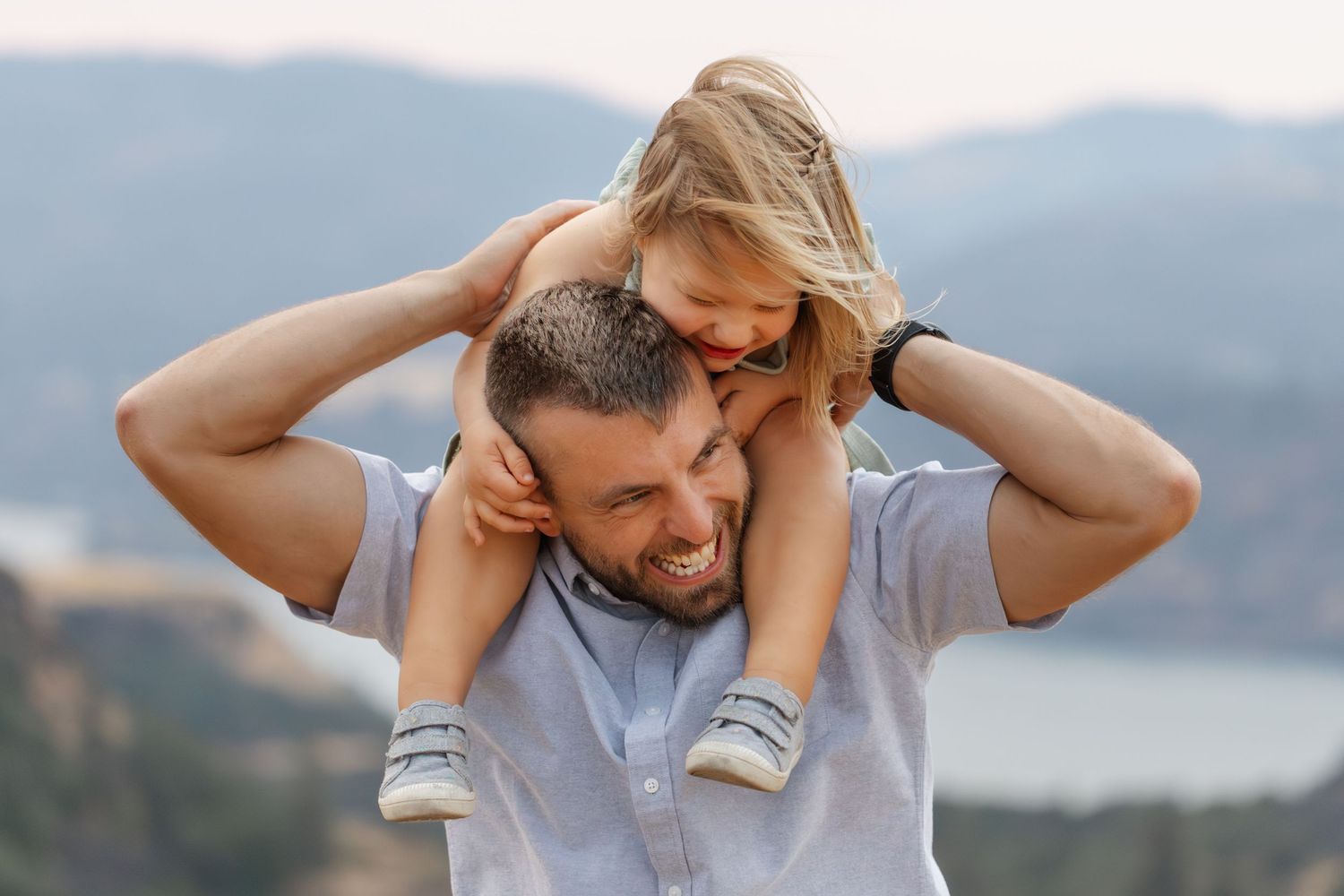 Parent and child share playful piggyback ride moments against mountain backdrop.