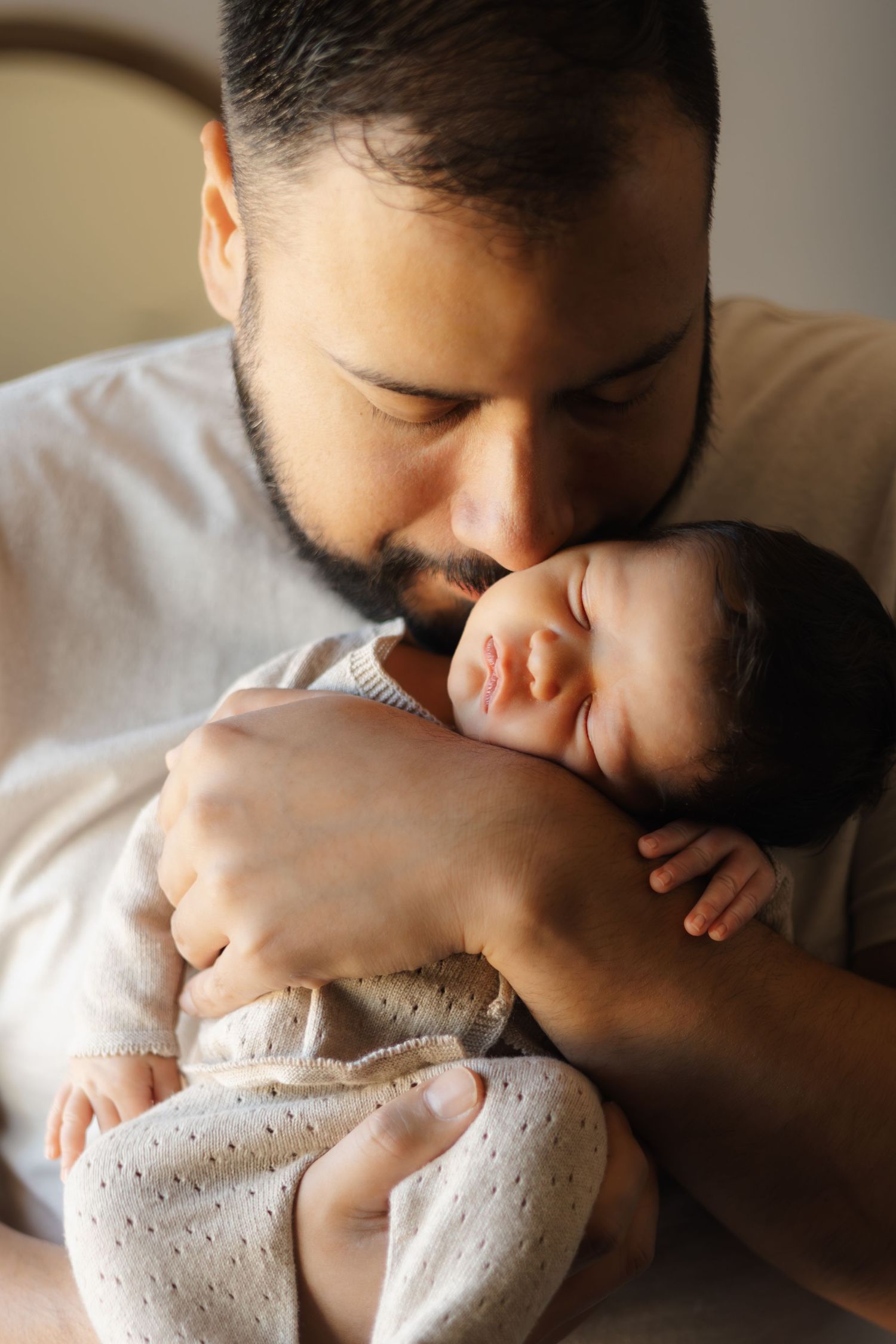 Parent giving gentle kiss to newborn baby in white clothing.
