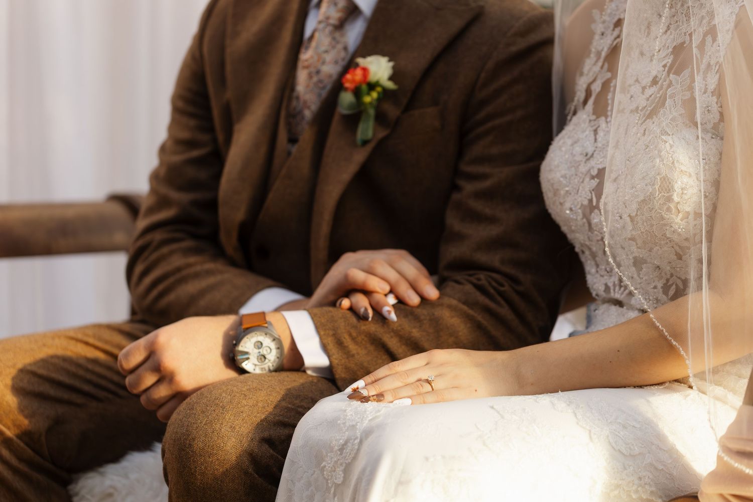 A couple sitting at a table holds hands during an intimate moment at what appears to be a wedding reception.