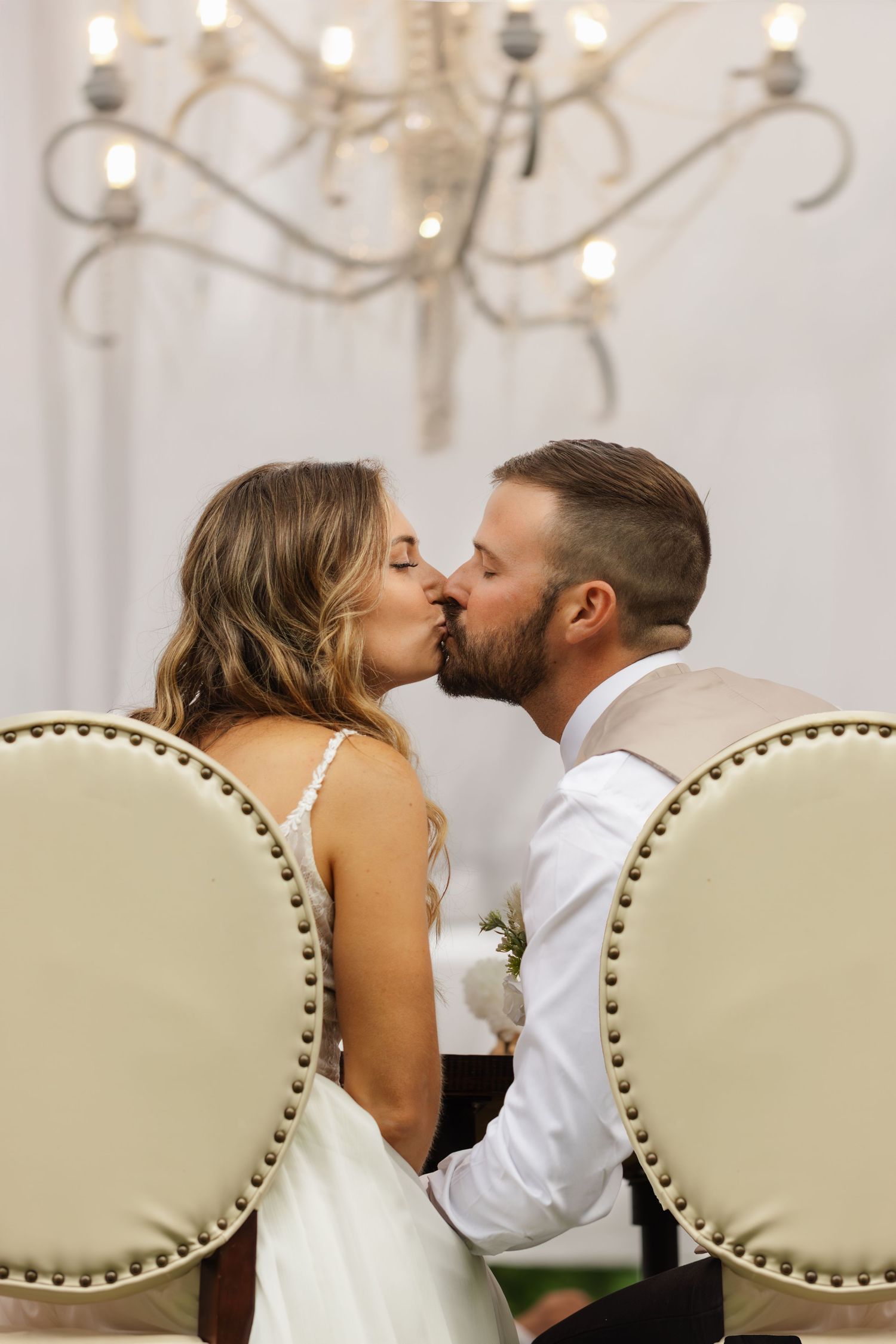 A romantic wedding kiss sequence showing five progressive moments between a couple seated on an upholstered chair.