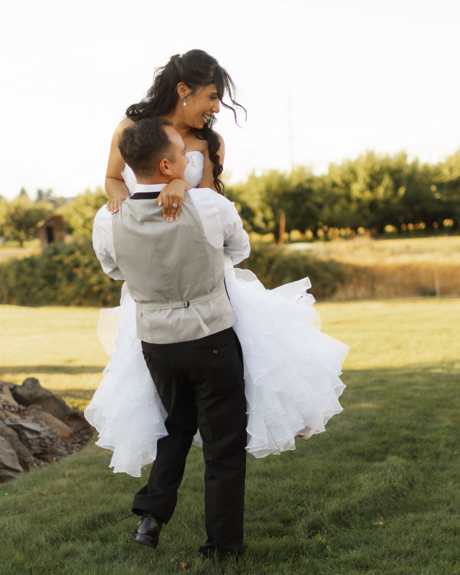 A couple embraces in a romantic dance pose on a grassy field during golden hour.