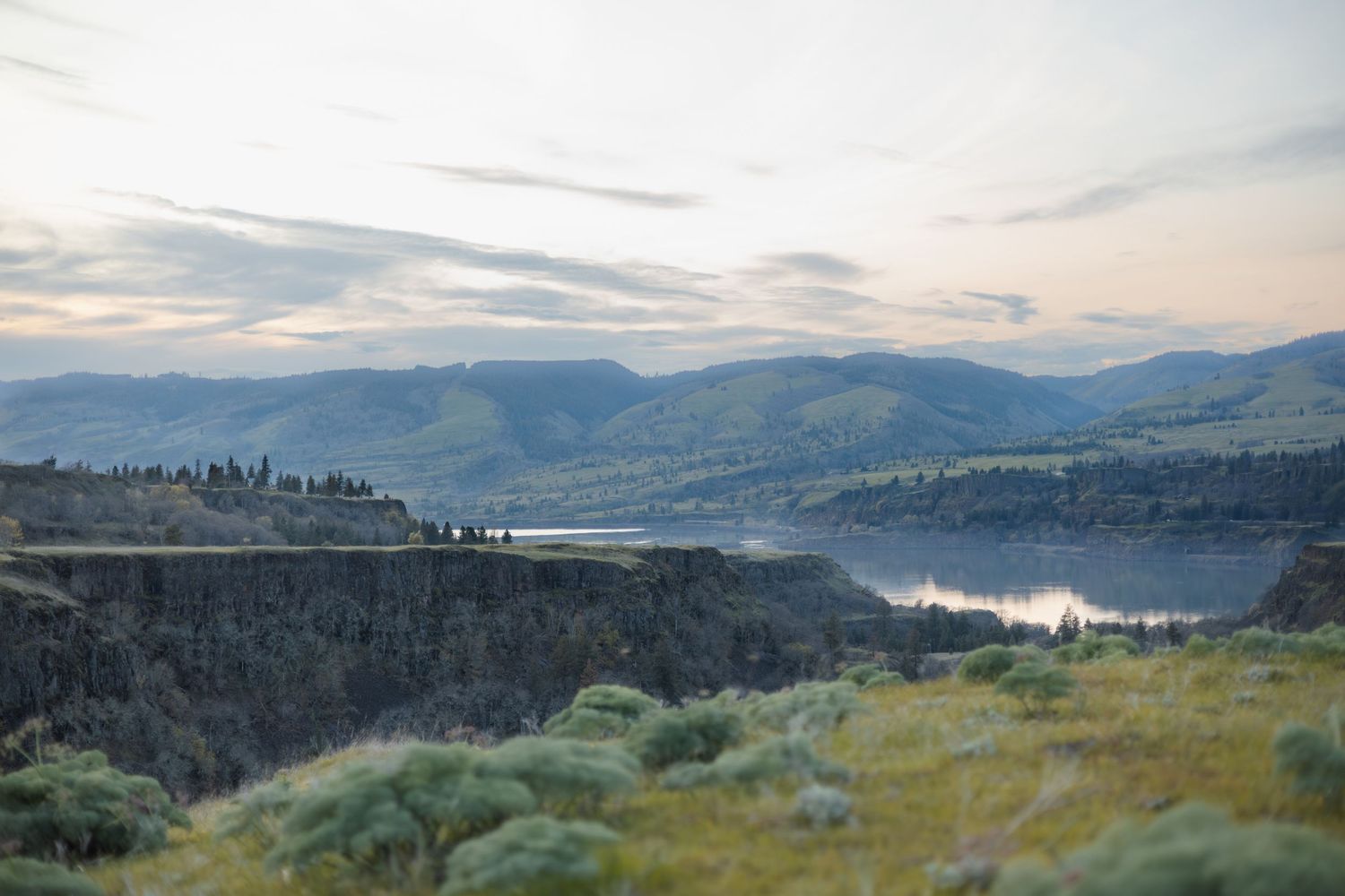 Scenic mountain landscape at dusk overlooking a lake with rolling hills and misty valleys in the background.