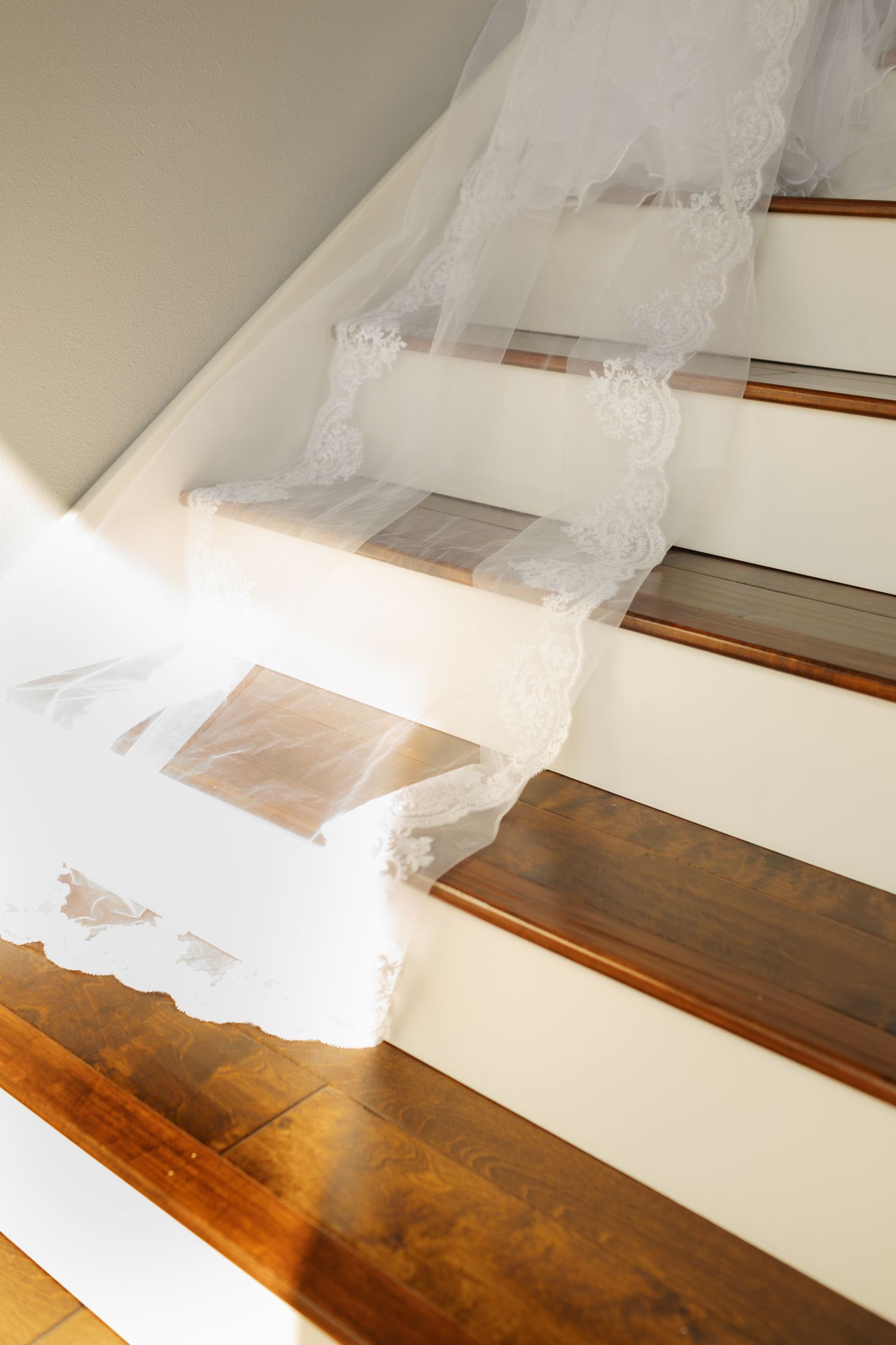 Flowing white wedding veil draped across wooden stairs in soft natural light.