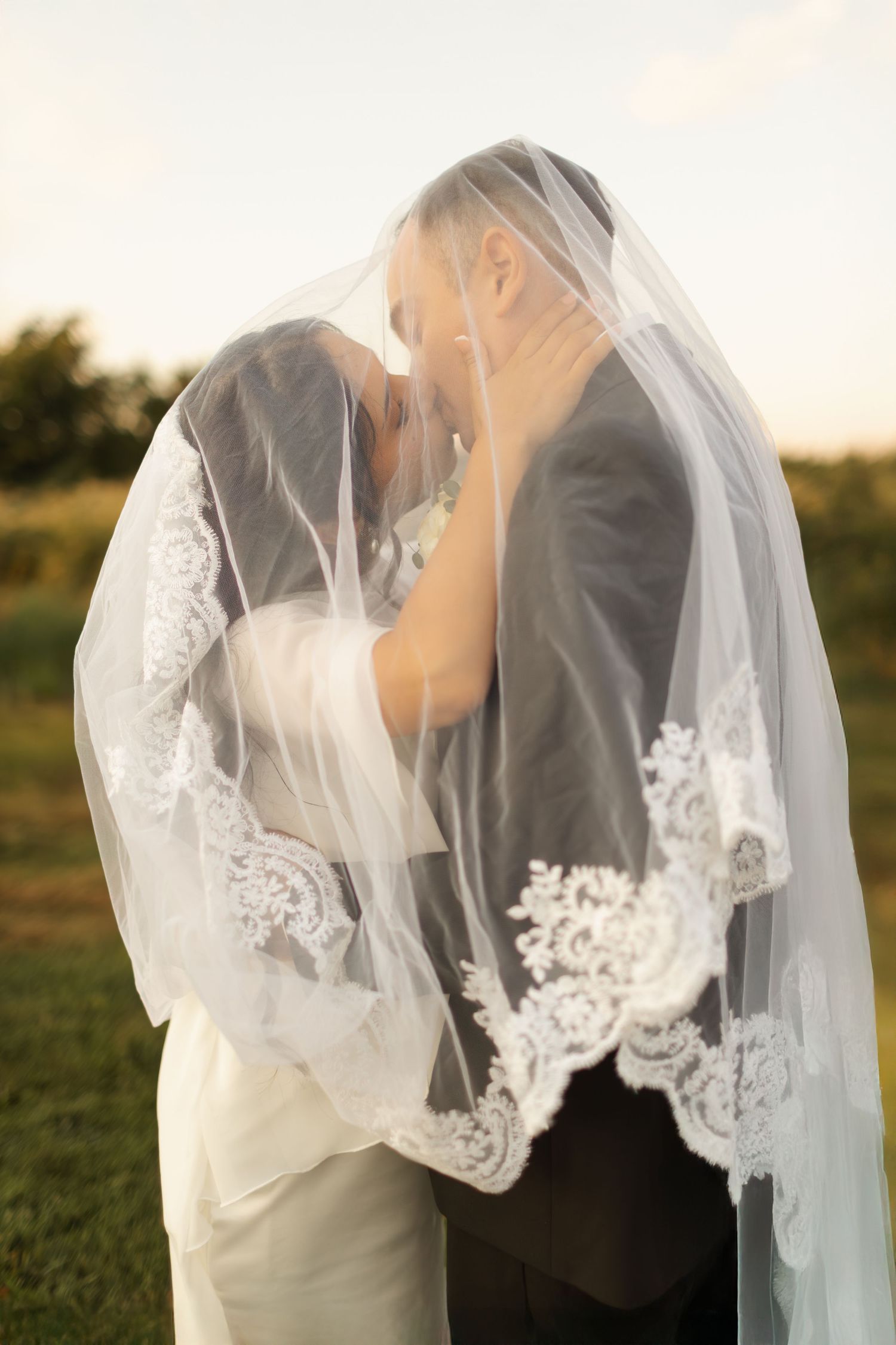 A romantic wedding moment captured under a delicate lace veil during golden hour.