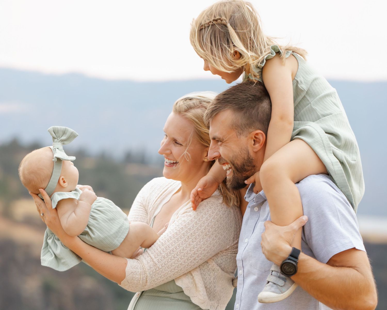 Family enjoying playful moment outdoors against mountain backdrop.