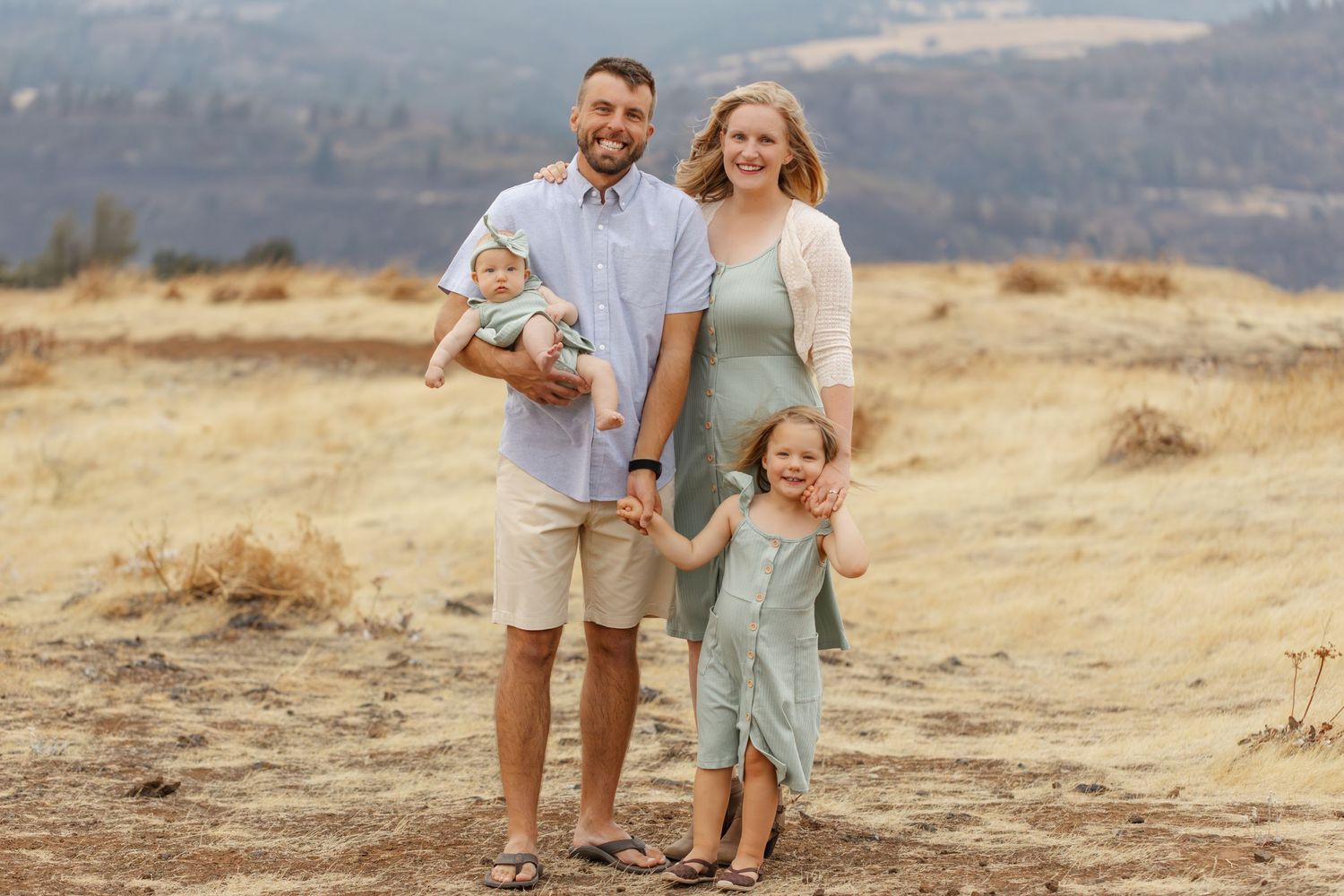 Family of four standing together on hilltop during golden hour.