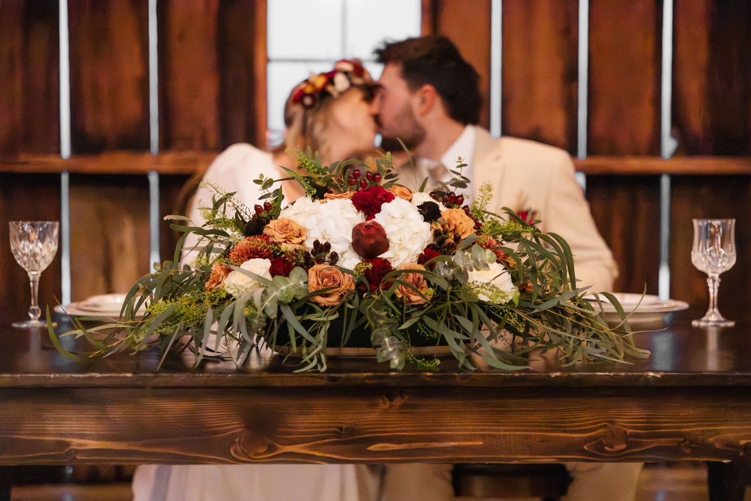 Rustic wedding table with beautiful autumn-toned floral centerpiece and wine glasses.