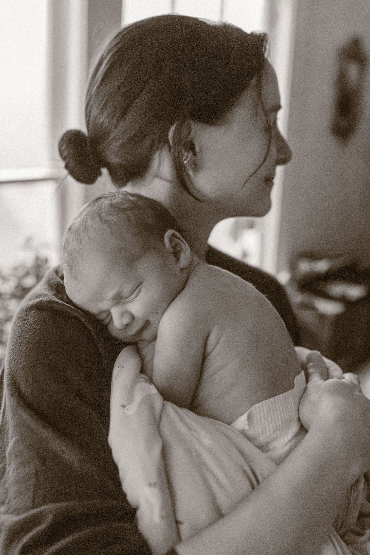 Black and white portrait of a mother tenderly cradling her sleeping newborn baby.