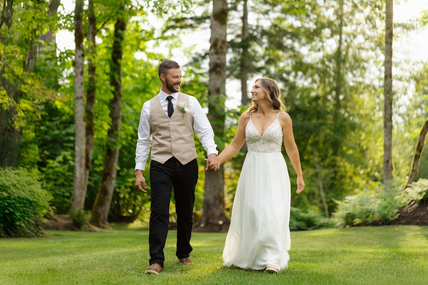 A couple walks hand in hand through a lush green garden setting on their wedding day.