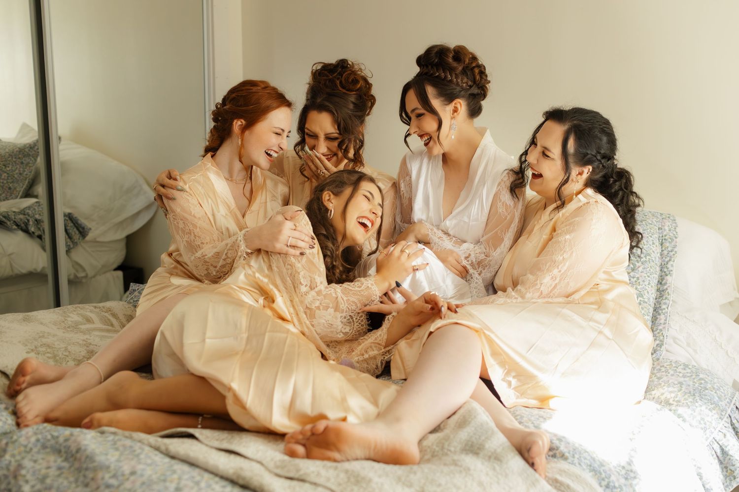 A group in matching silk robes share joyful laughter while relaxing together on a bed.