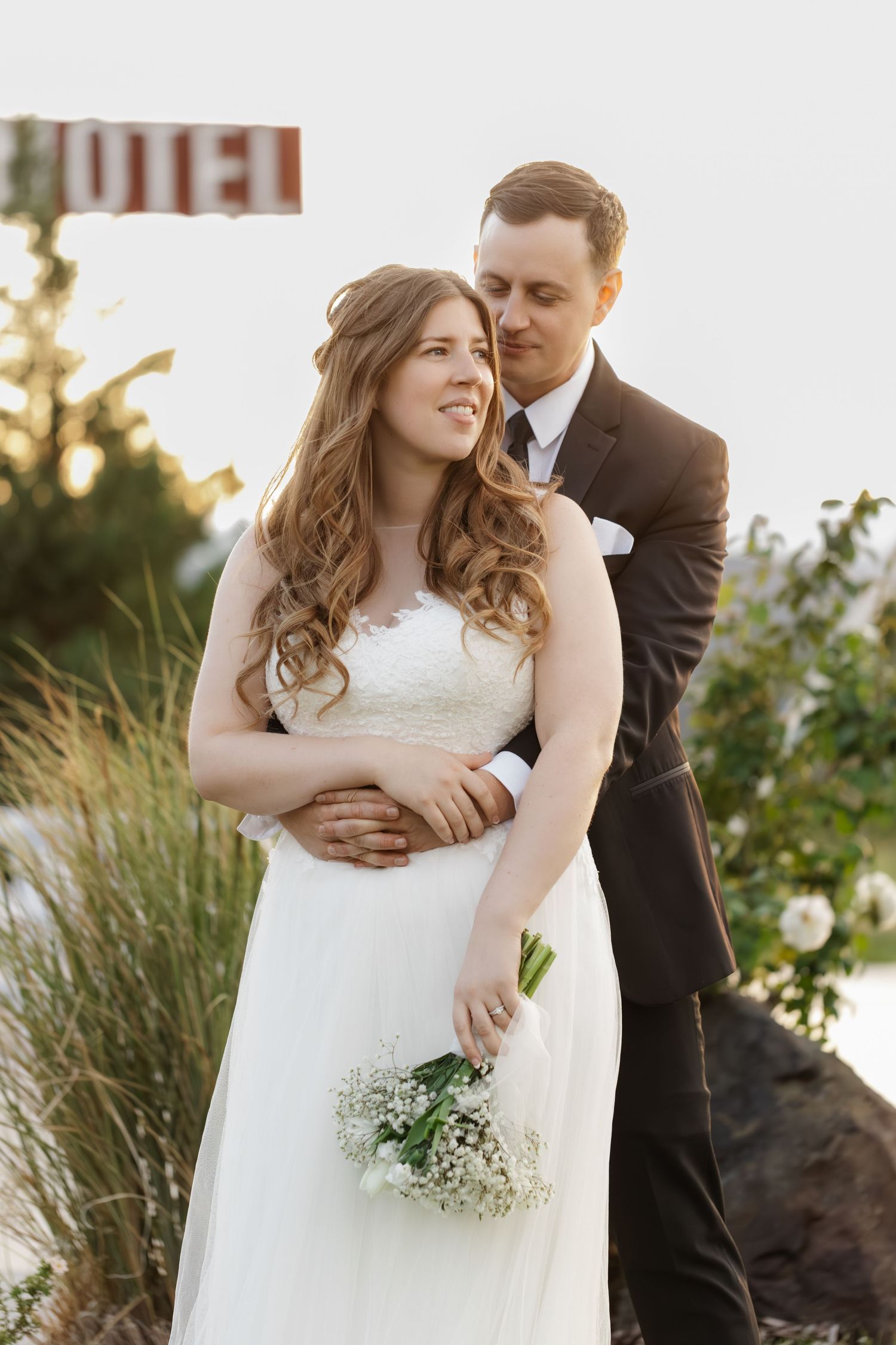 Romantic wedding couple embraces while holding a delicate bouquet of baby's breath flowers at sunset.