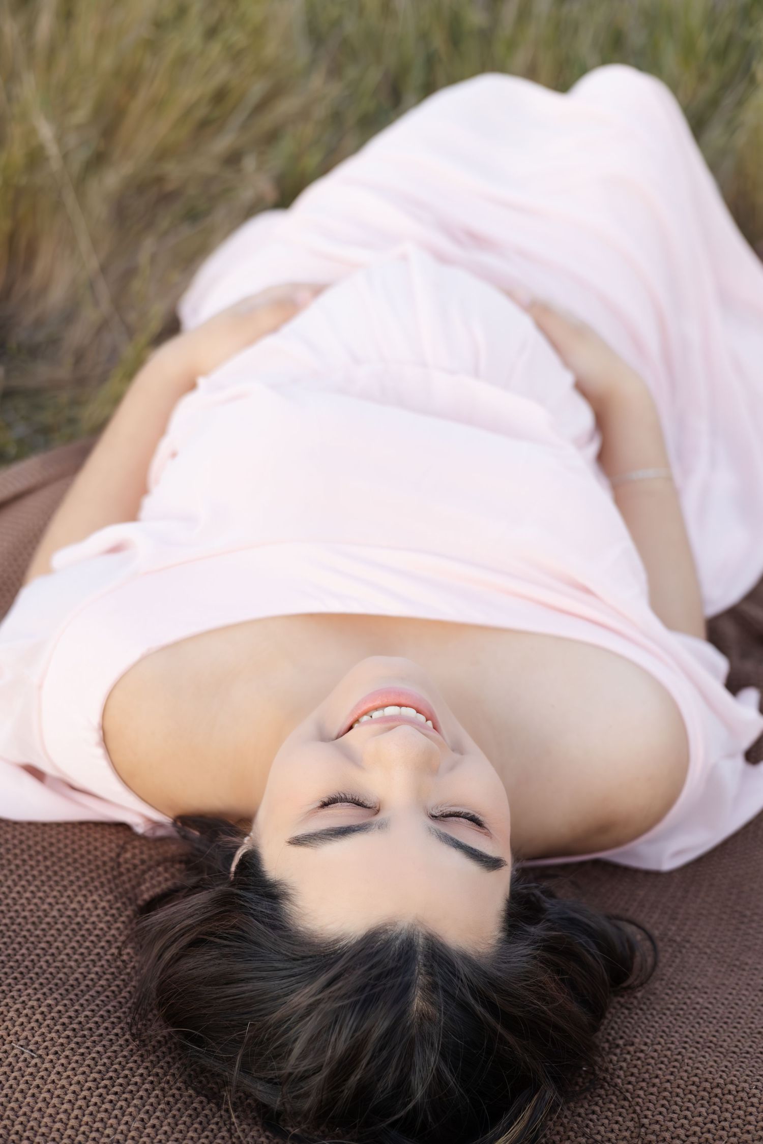 Person in light pink dress lying on blanket outdoors with peaceful expression.