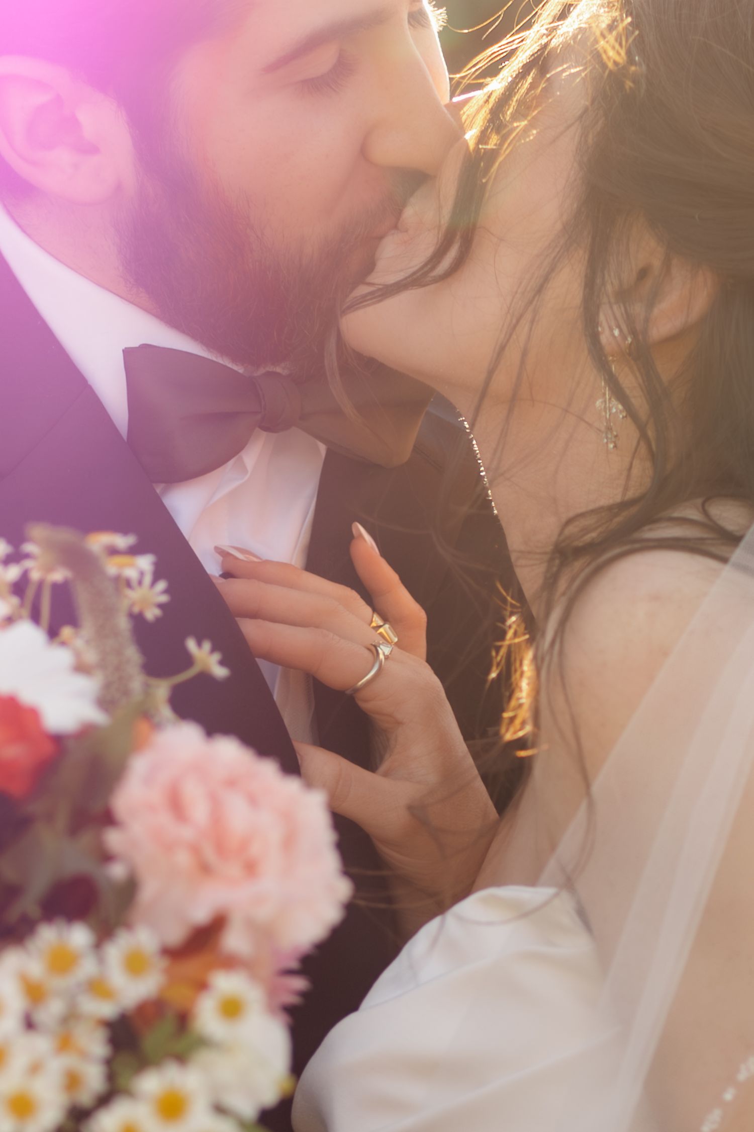 Wedding couple embracing with pink lighting and white daisies in the background.