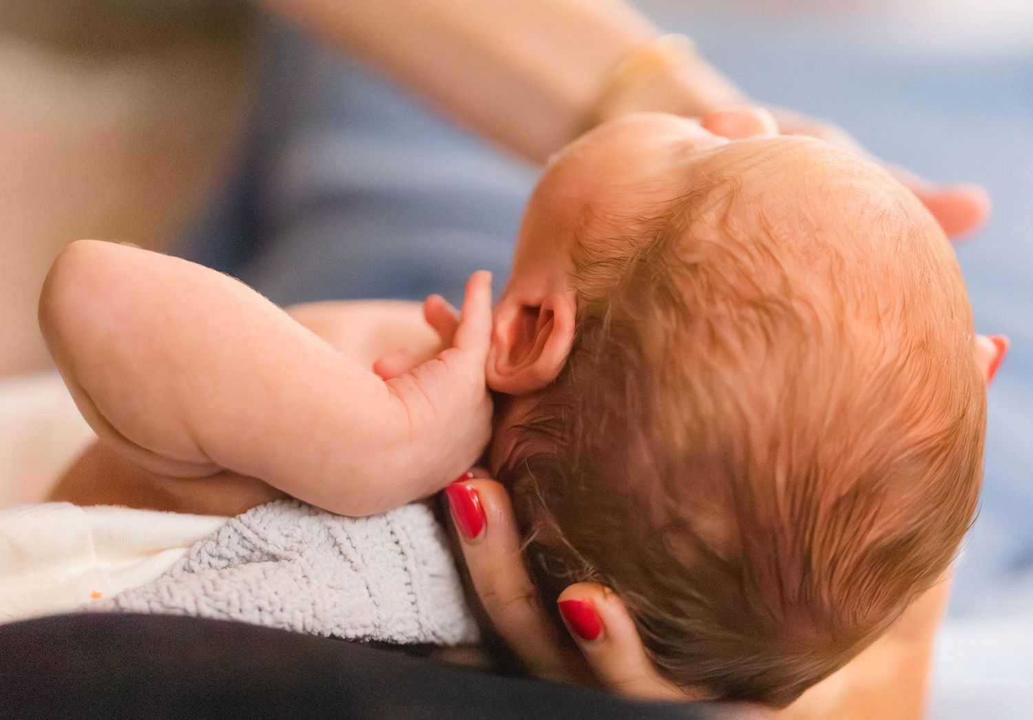 Close-up of a newborn baby being cradled in mother's arms during breastfeeding, showing infant's delicate features.