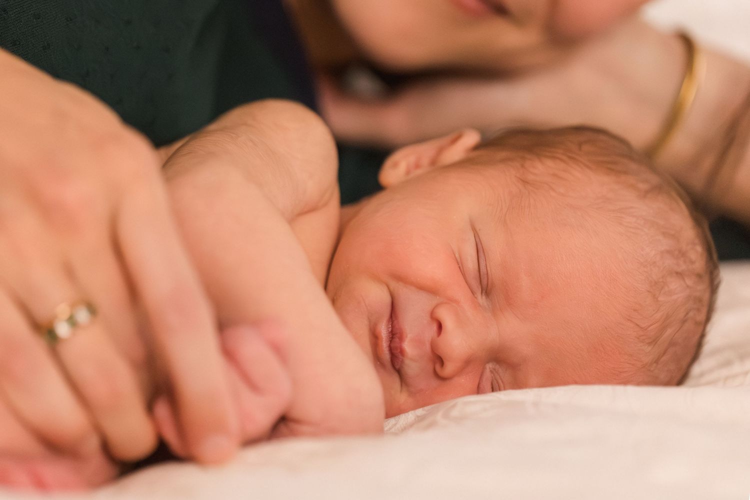 Newborn baby smiling while sleeping on a white blanket, held gently by parents in a tender moment.