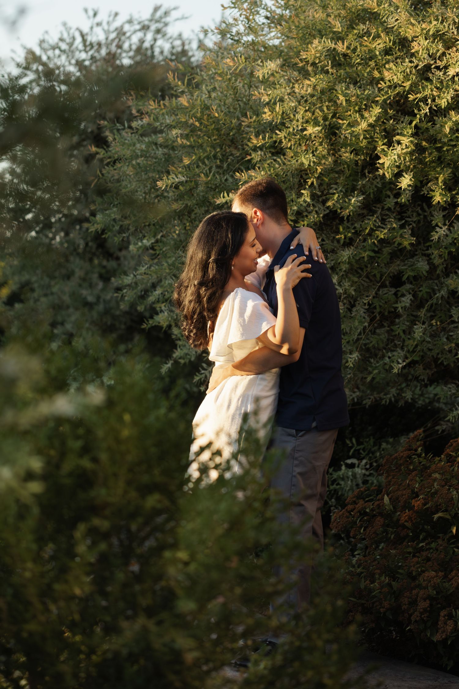 Couple sharing romantic moment among green foliage in natural setting.