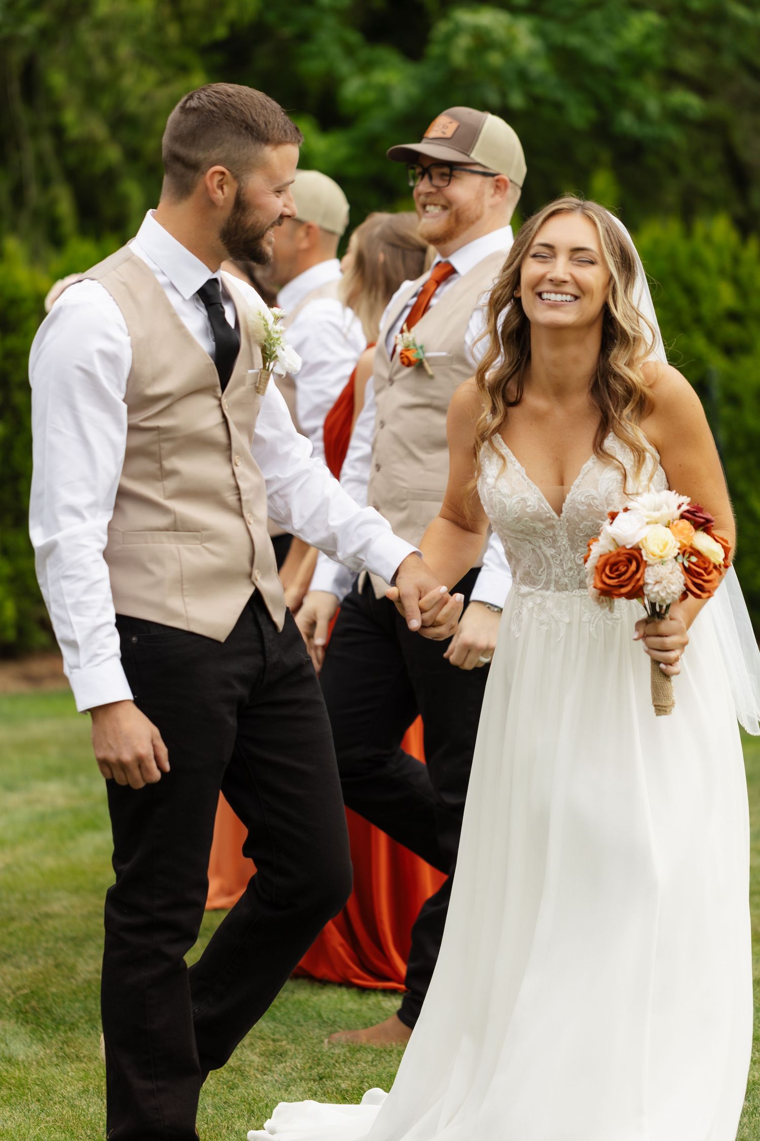 Wedding party members laugh and celebrate together outdoors against a green natural backdrop.