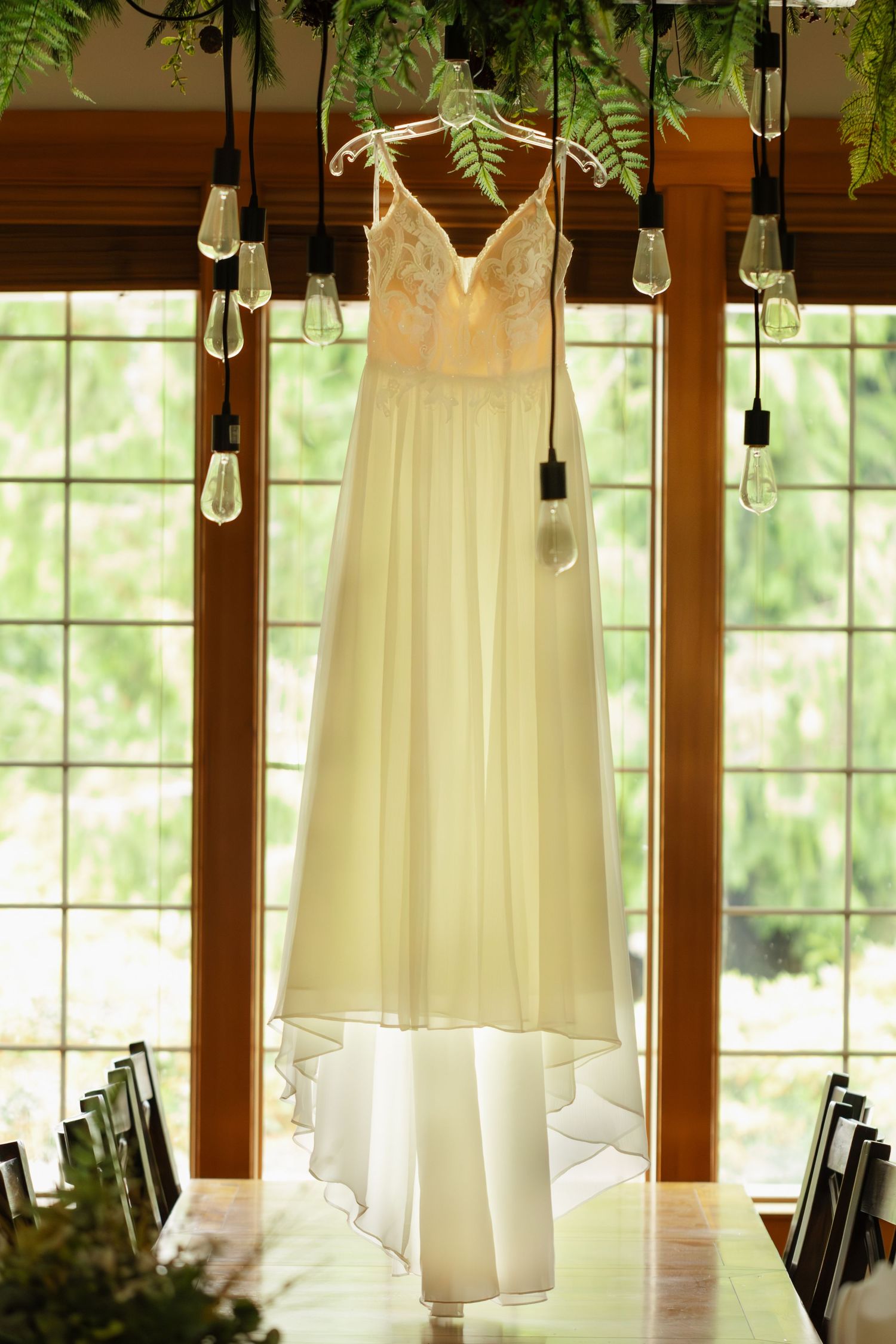 White wedding dresses hanging from wooden beams in a rustic venue with natural light streaming through windows.