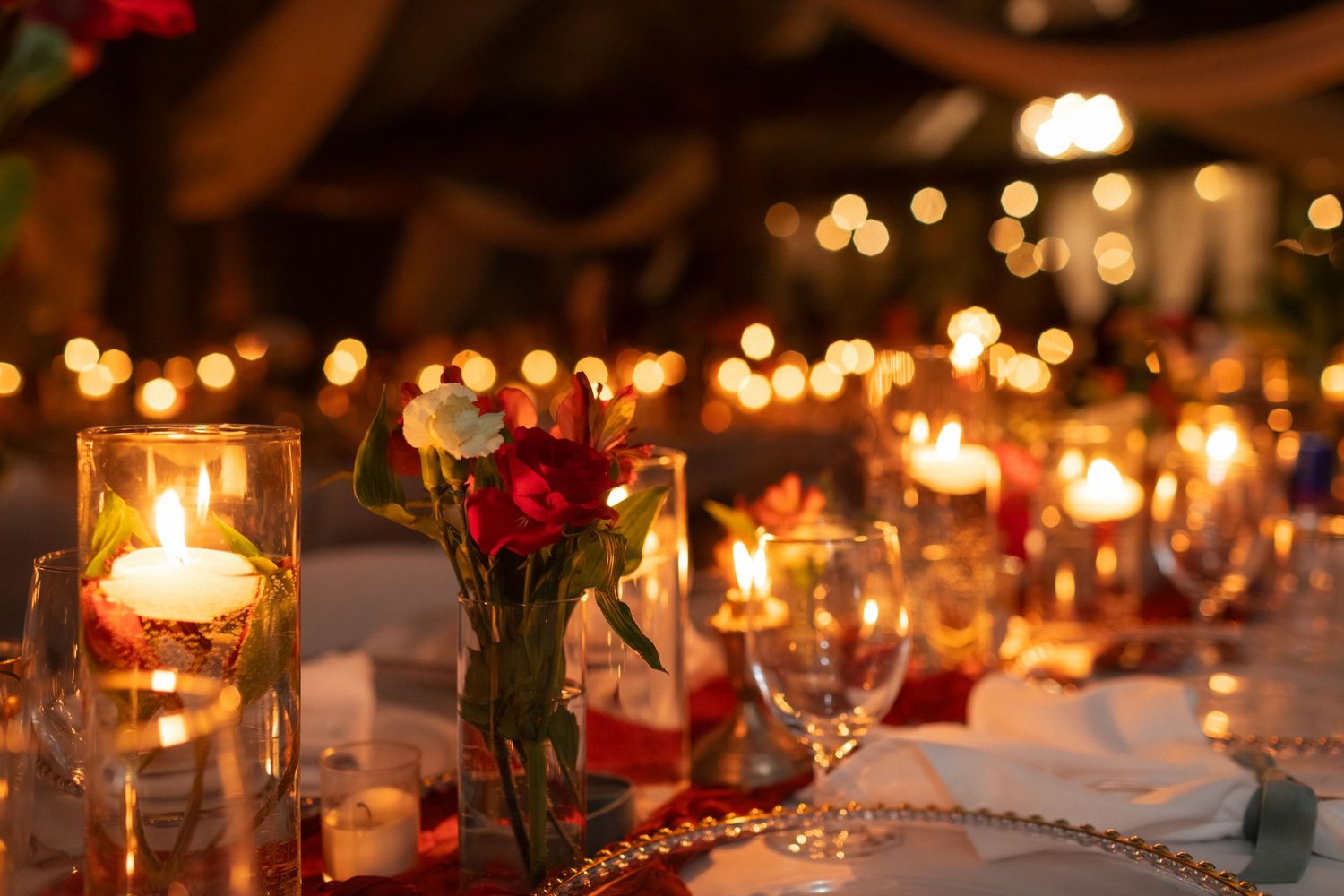 Romantic candlelit wedding reception table with red flowers and glowing ambiance.