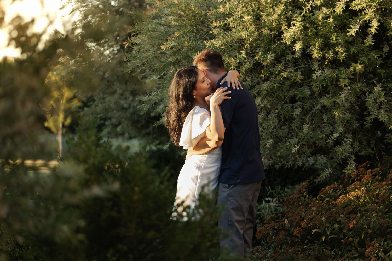 Romantic couple embracing at sunset with green foliage background.