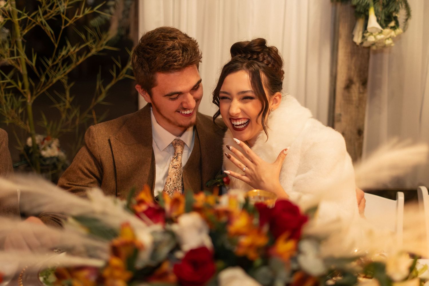A couple shares an intimate moment during their wedding reception surrounded by floral decorations and warm lighting.