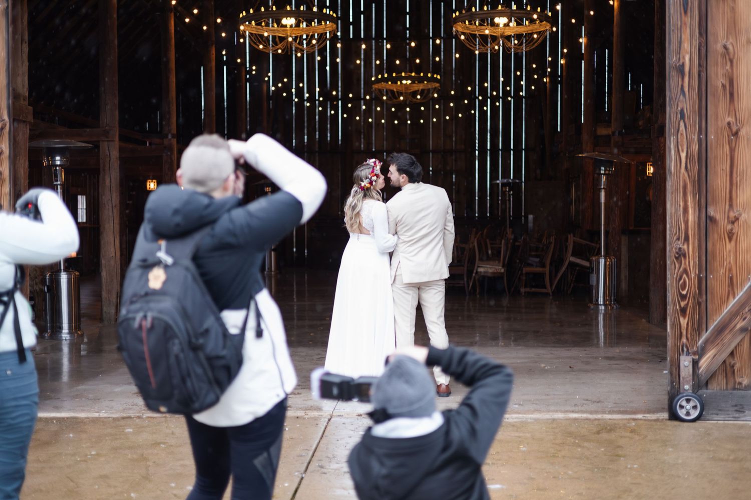 Wedding photographers capture a ceremony under twinkling lights in a rustic venue.