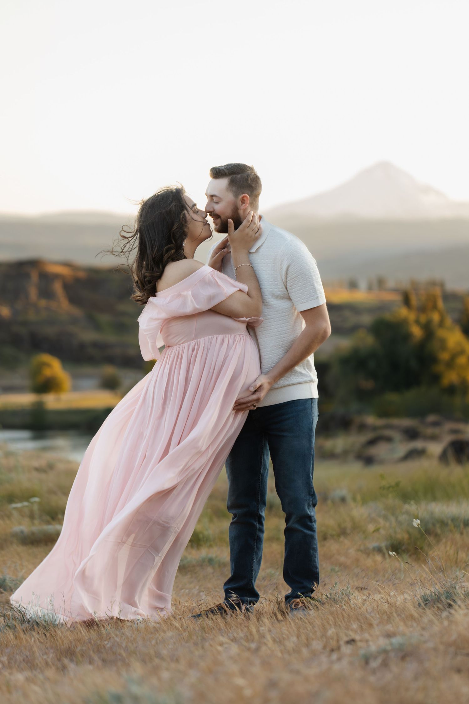 Romantic embrace in pink flowing dress against mountain landscape.