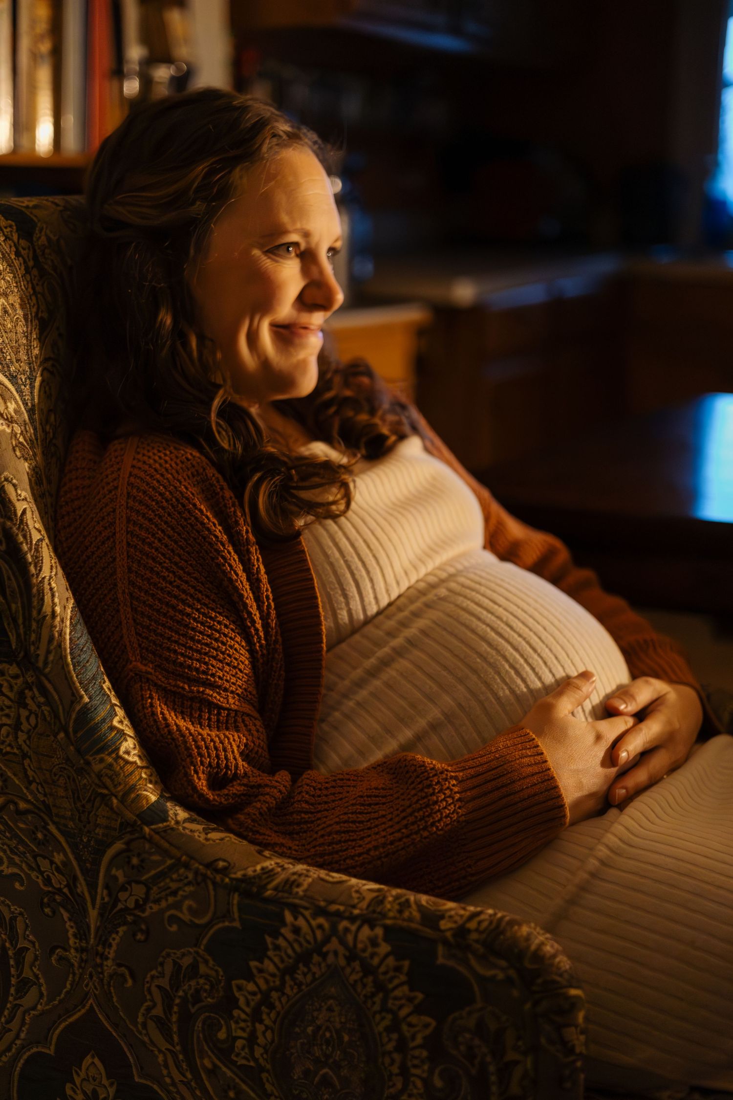 Cozy indoor maternity photo with warm lighting and brown knit sweater.