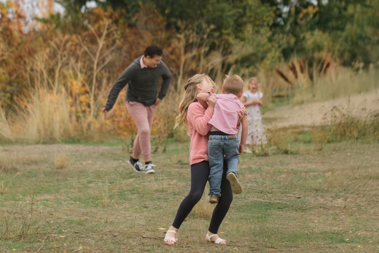 Children playing outdoors in a grassy field surrounded by autumn trees, laughing and running together on a sunny day.