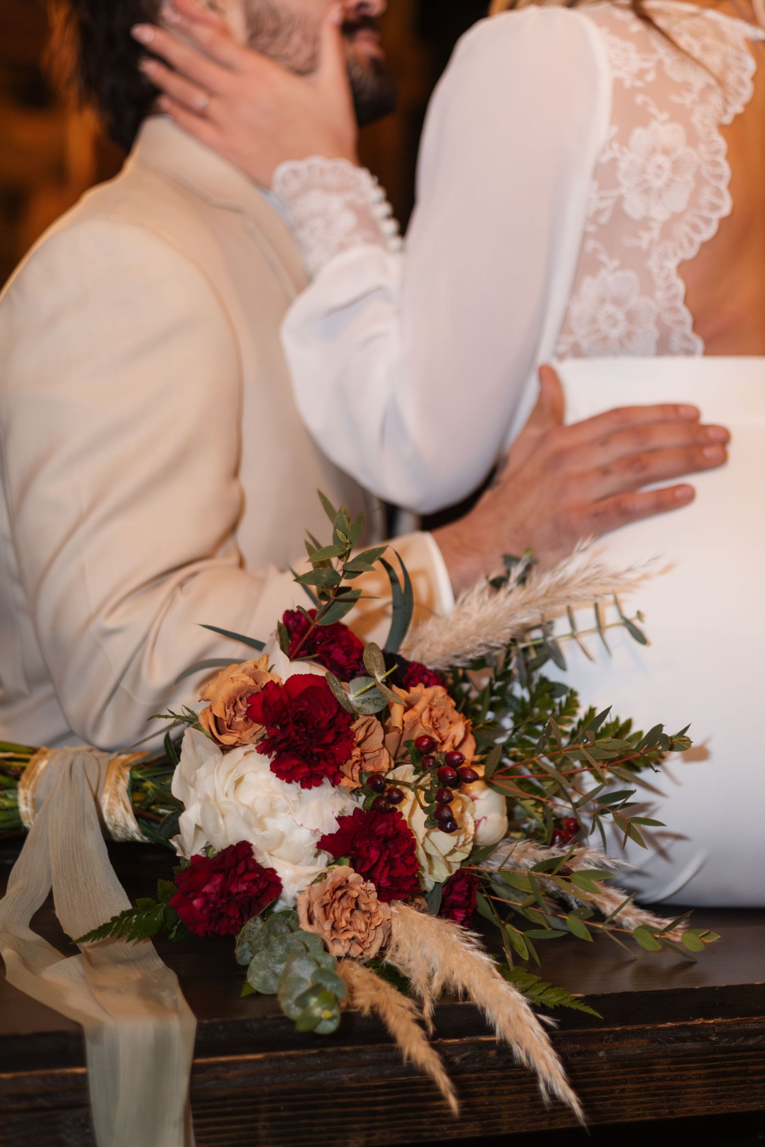 Elegant bridal bouquet with deep red and peach flowers against white wedding dress.
