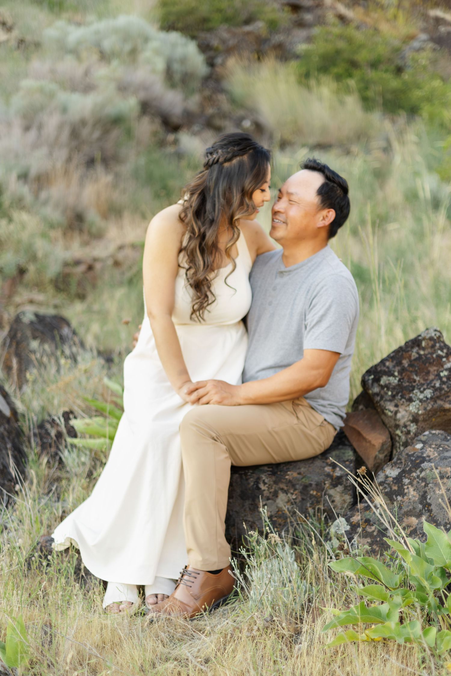 Romantic couple sitting together on rocky terrain surrounded by green grass and natural landscape.