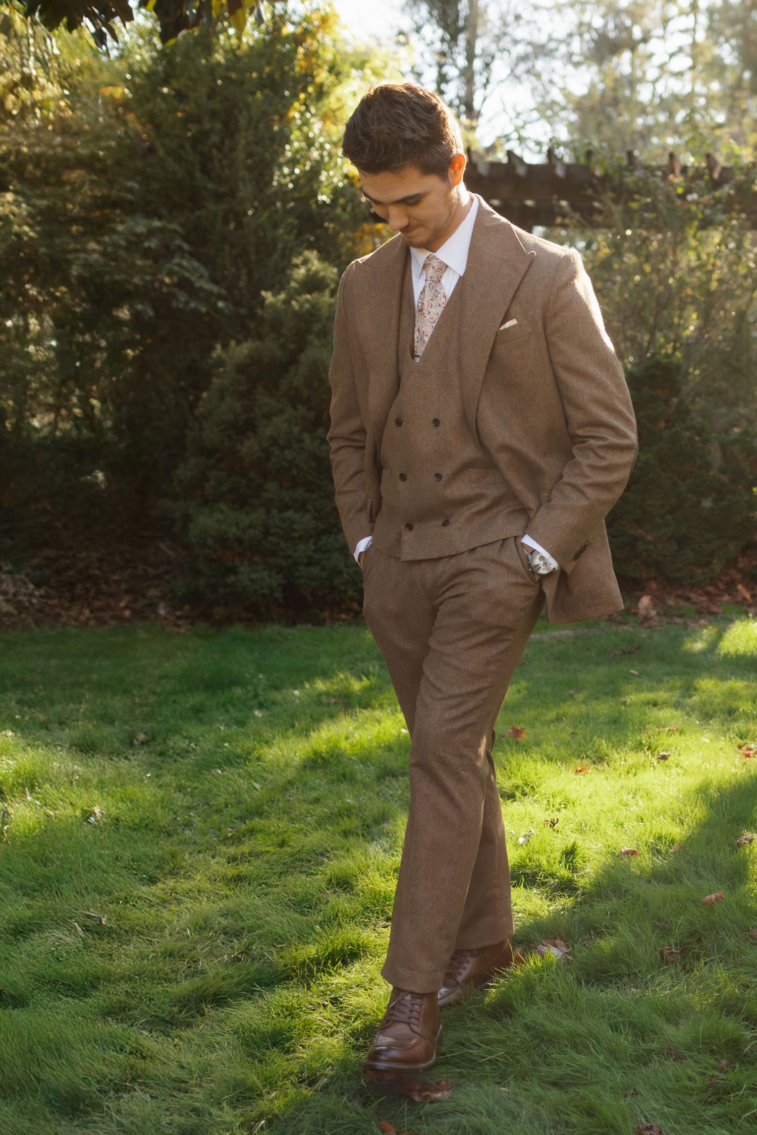 A figure in a brown suit strikes playful poses in a grassy outdoor setting with sunlit trees in the background.