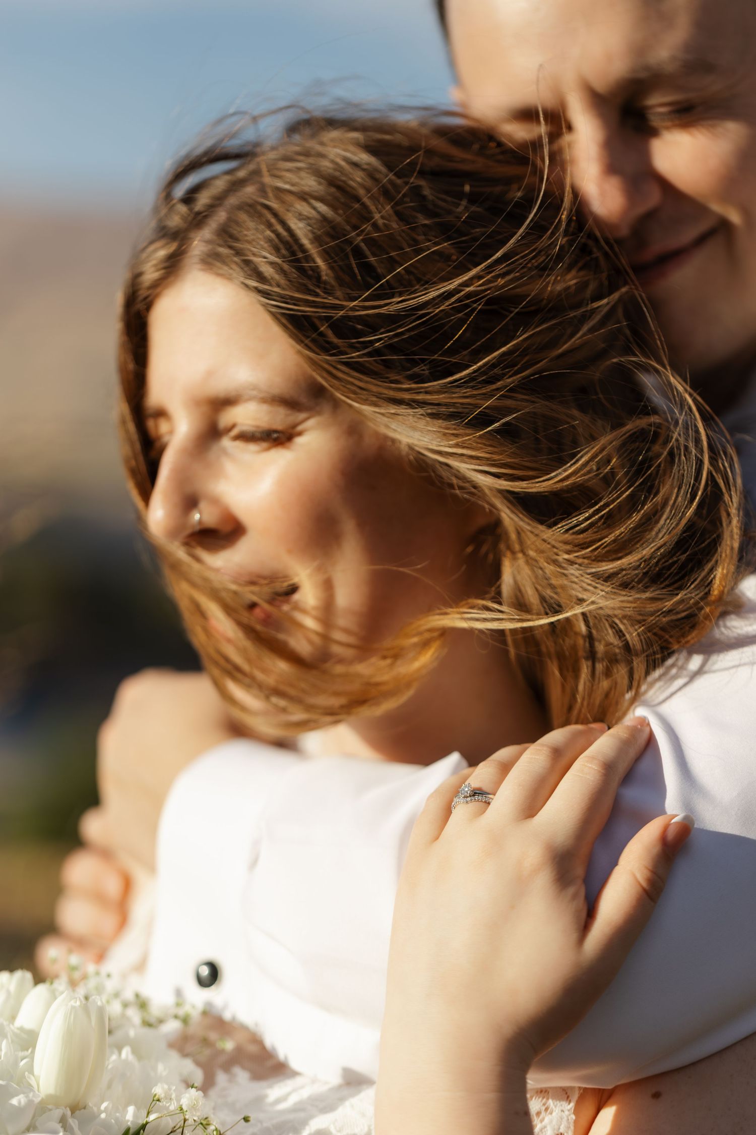 Romantic close-up portrait of a couple embracing with wind blowing through her hair while holding a white bouquet.