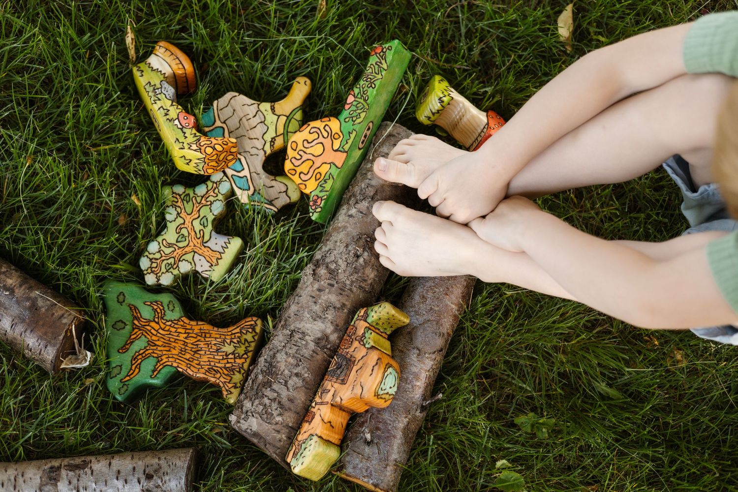Hands arranging decorative wooden objects on grass outdoors.