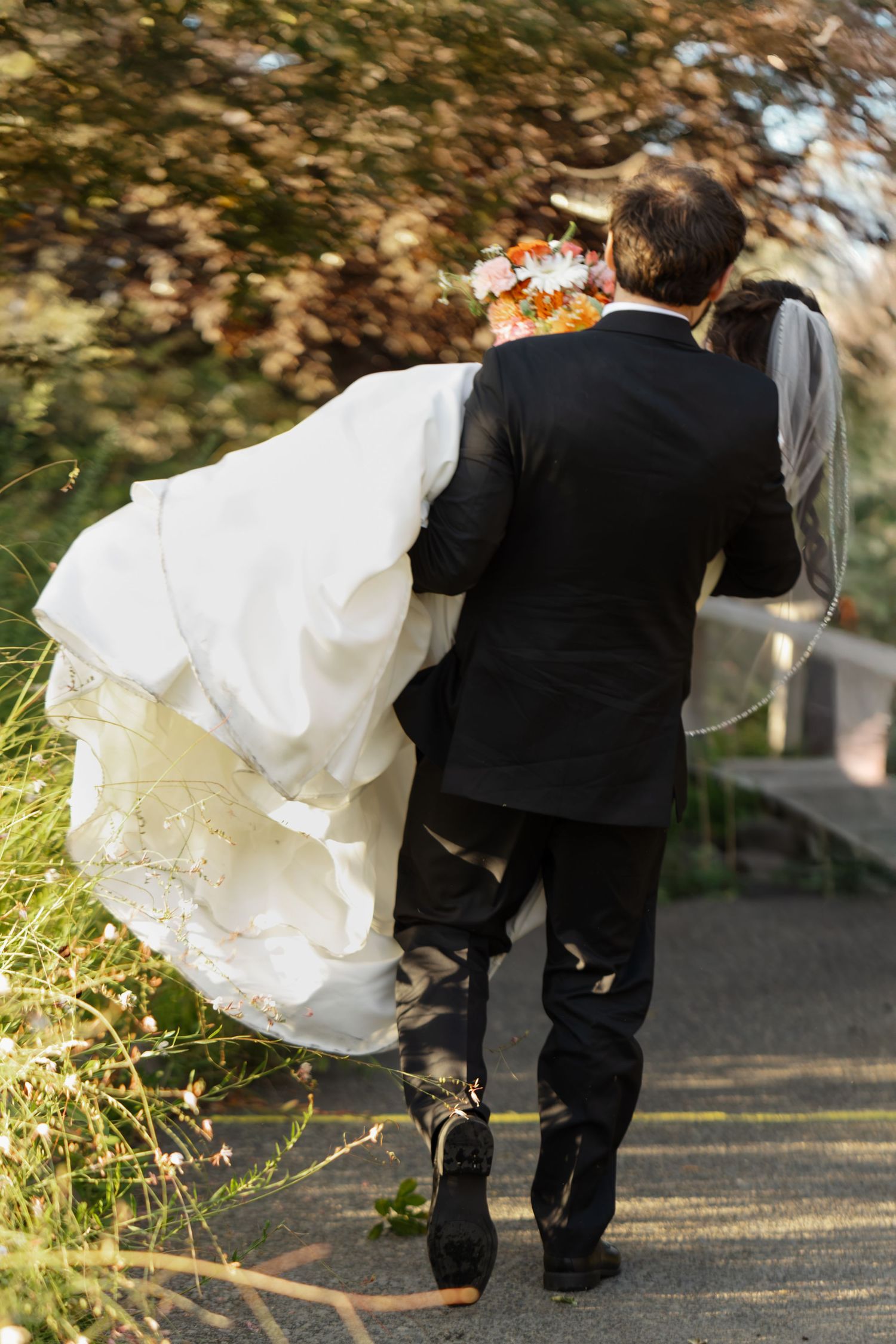 Wedding couple walking away on a garden path with bride's white dress flowing in the breeze.